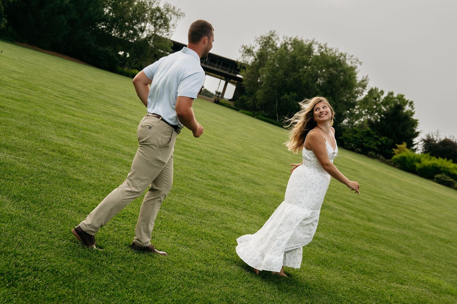 A couple in wedding attire dances playfully across a green lawn on their special day.