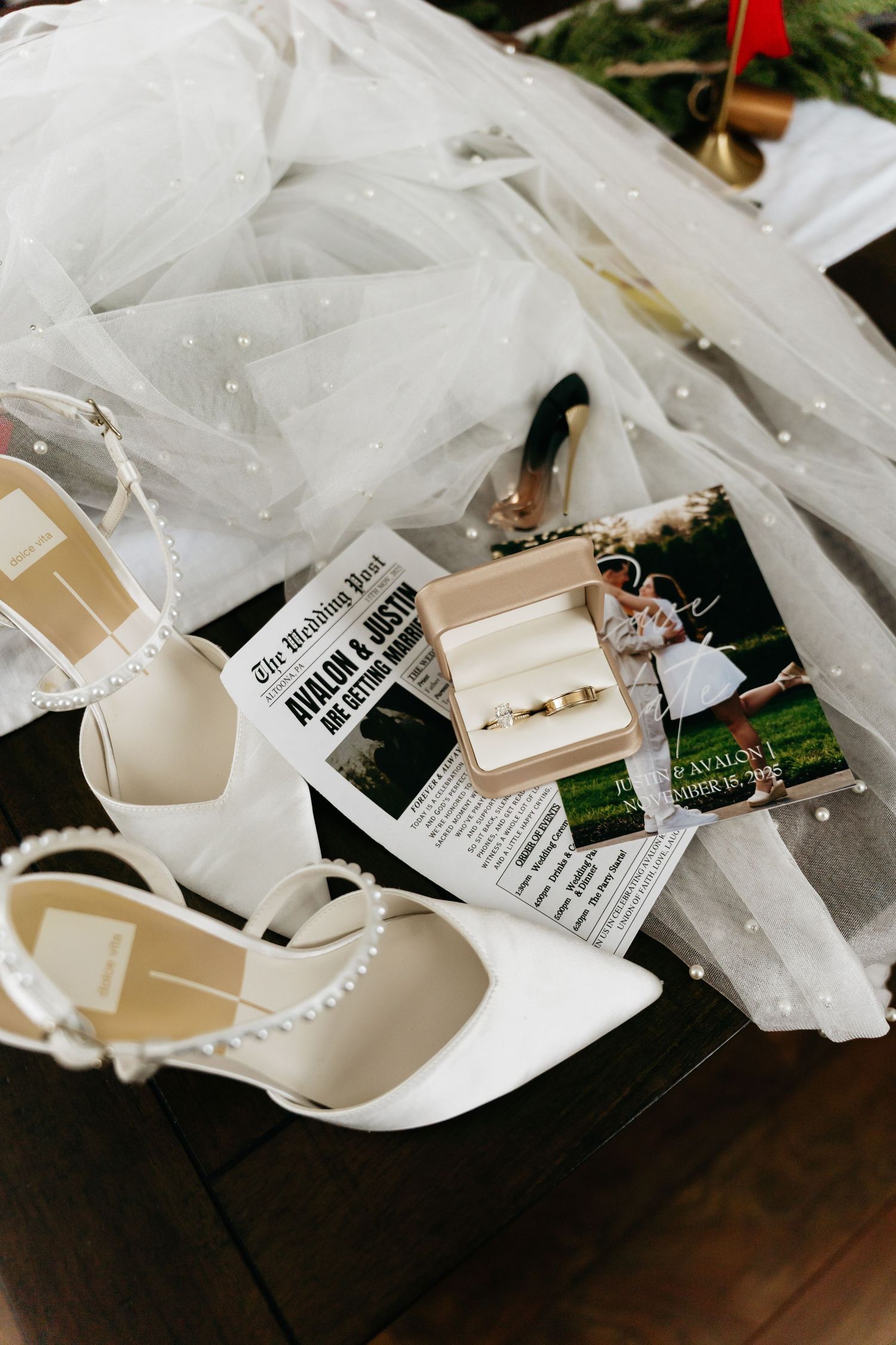 White bridal shoes and veil with price tags and wedding details arranged on dark wooden surface.