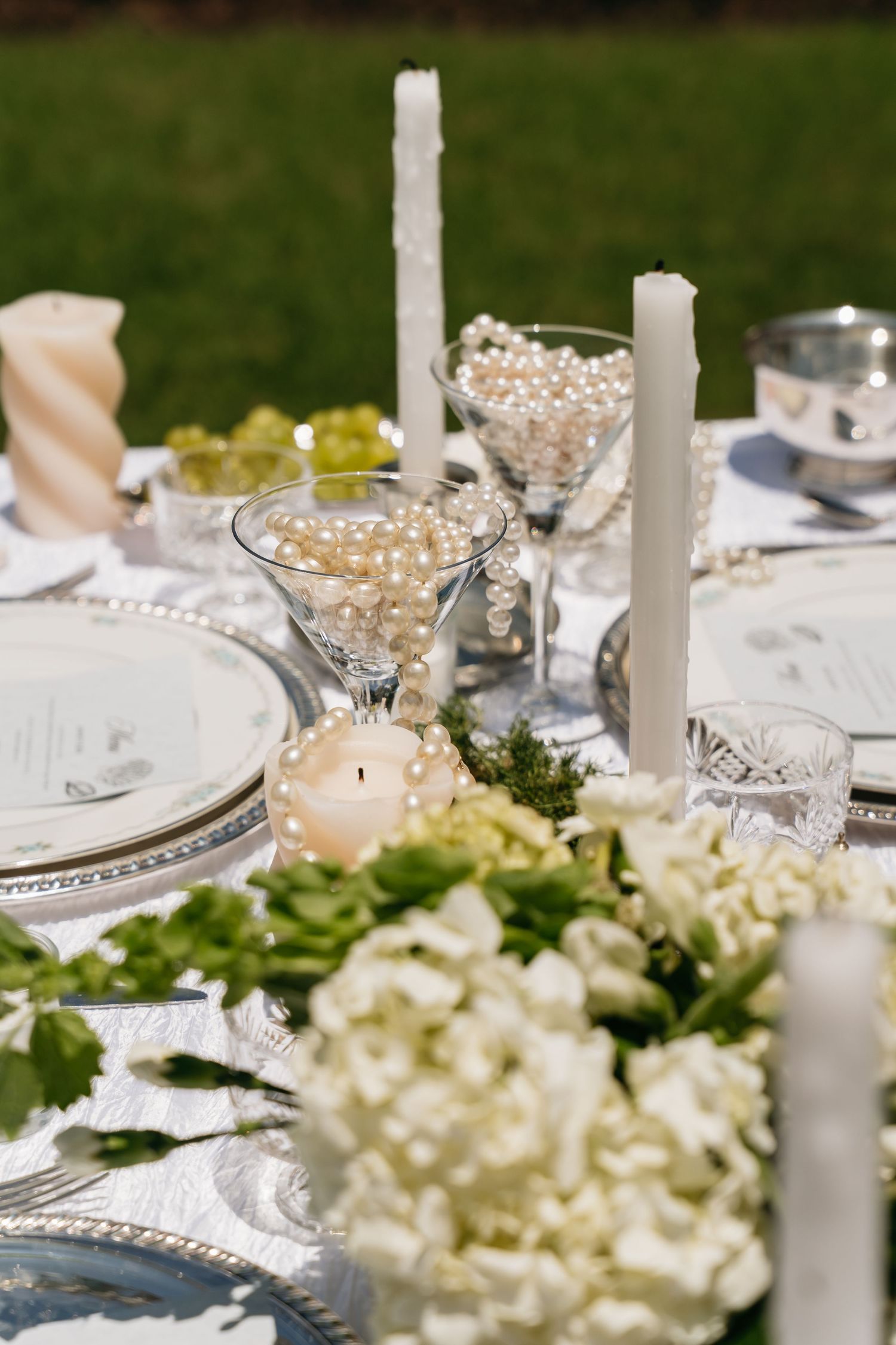 Elegant wedding table setting with white flowers, silver charger plates, crystal glassware and tall white candles.