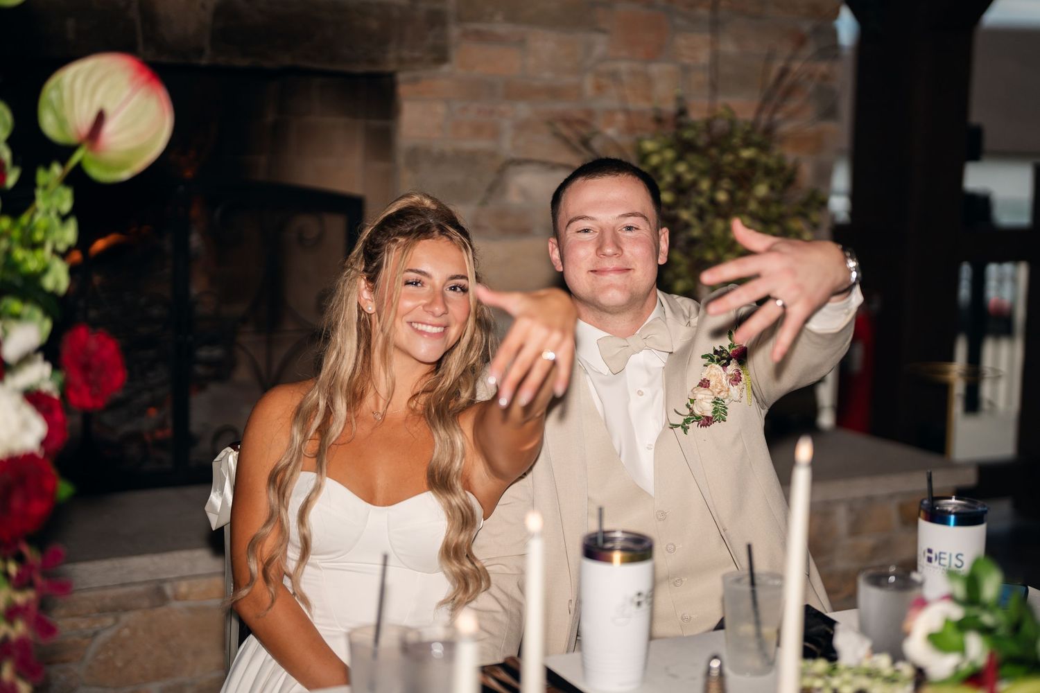 Bride and groom taking a selfie at their wedding reception, smiling joyfully near a stone fireplace.