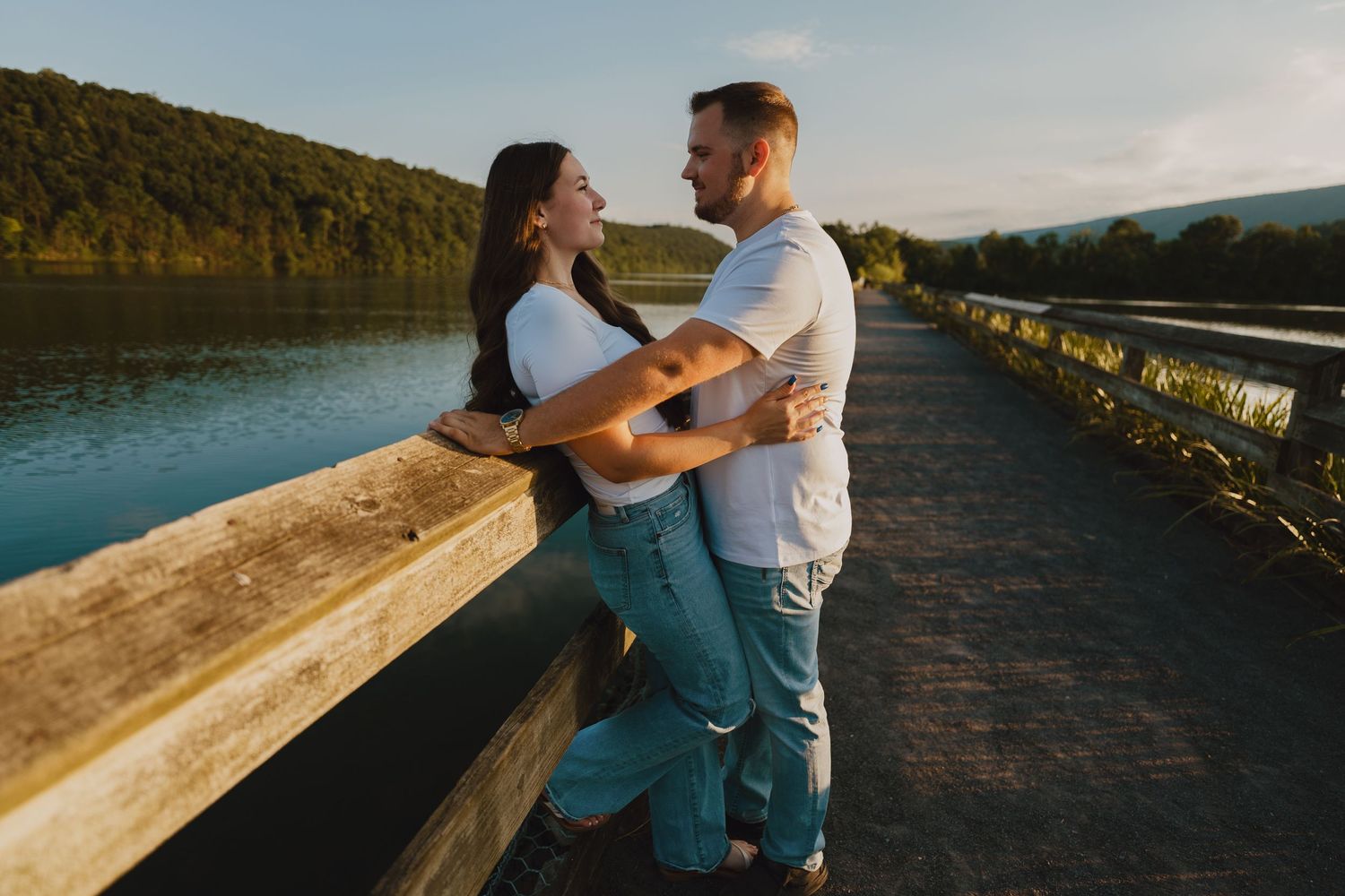 A couple embraces on a wooden boardwalk by a scenic lake during golden hour.