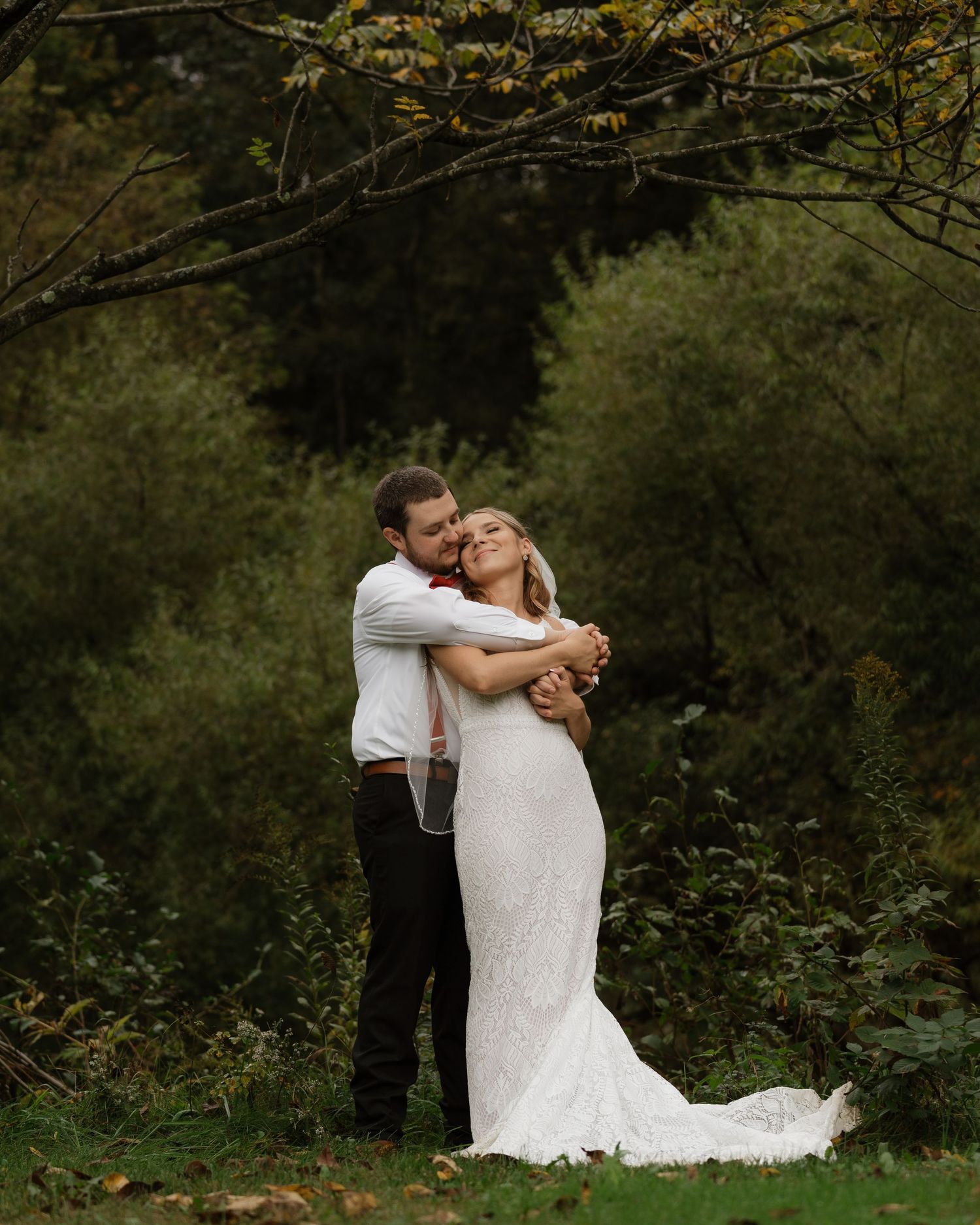 Romantic wedding couple dancing and embracing in a lush green forest setting.