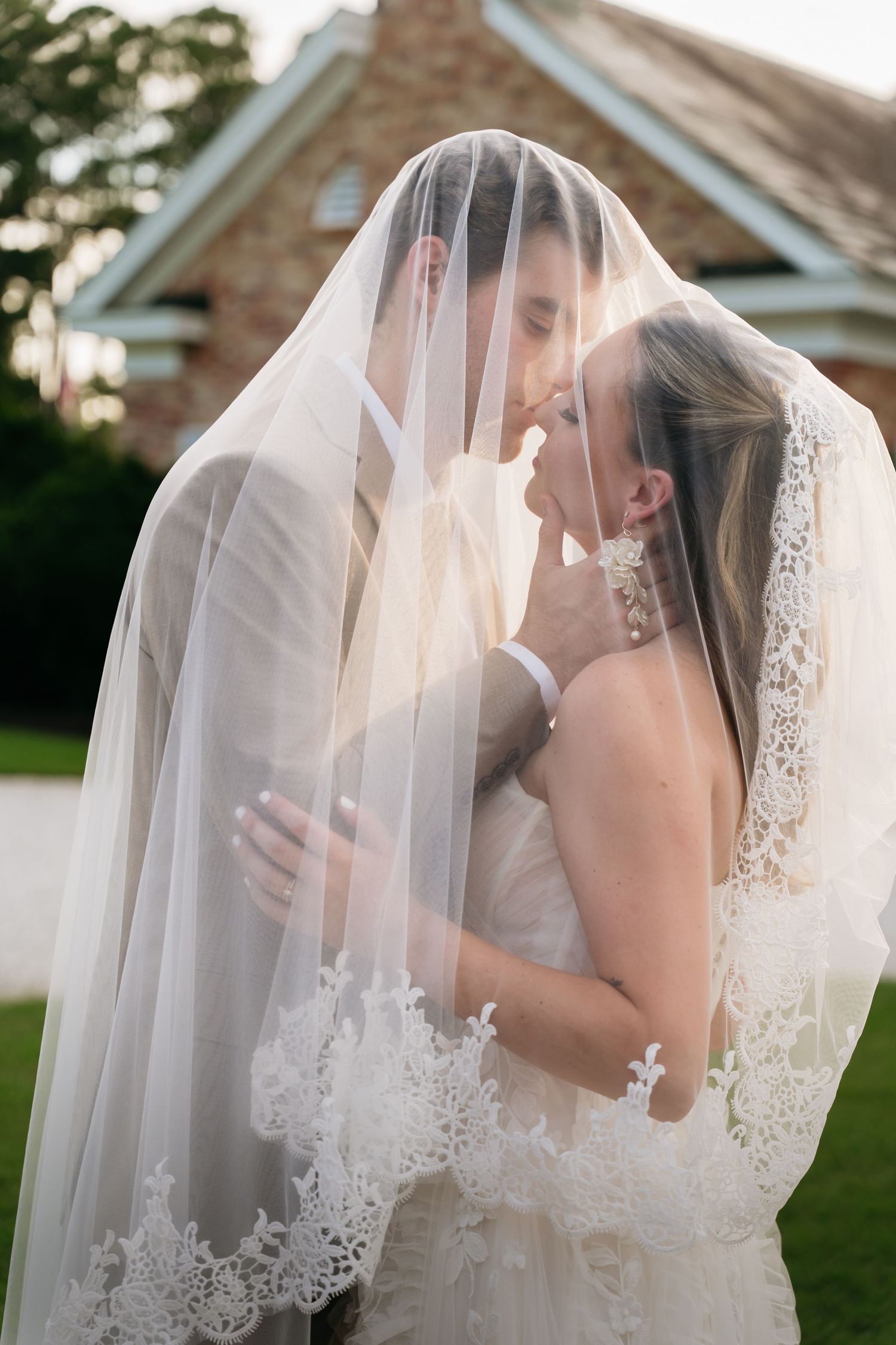 Bride and groom sharing a romantic kiss under a lace wedding veil outdoors near a stone building.