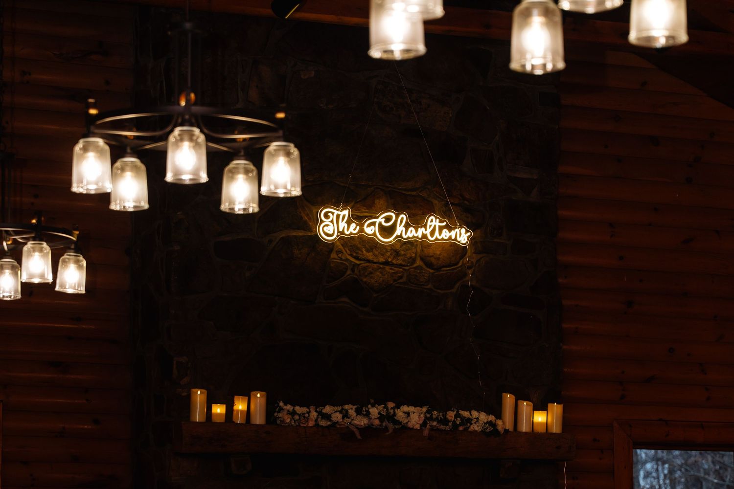 Warm neon sign reading The Charltons glows on dark stone wall with elegant hanging glass lights.