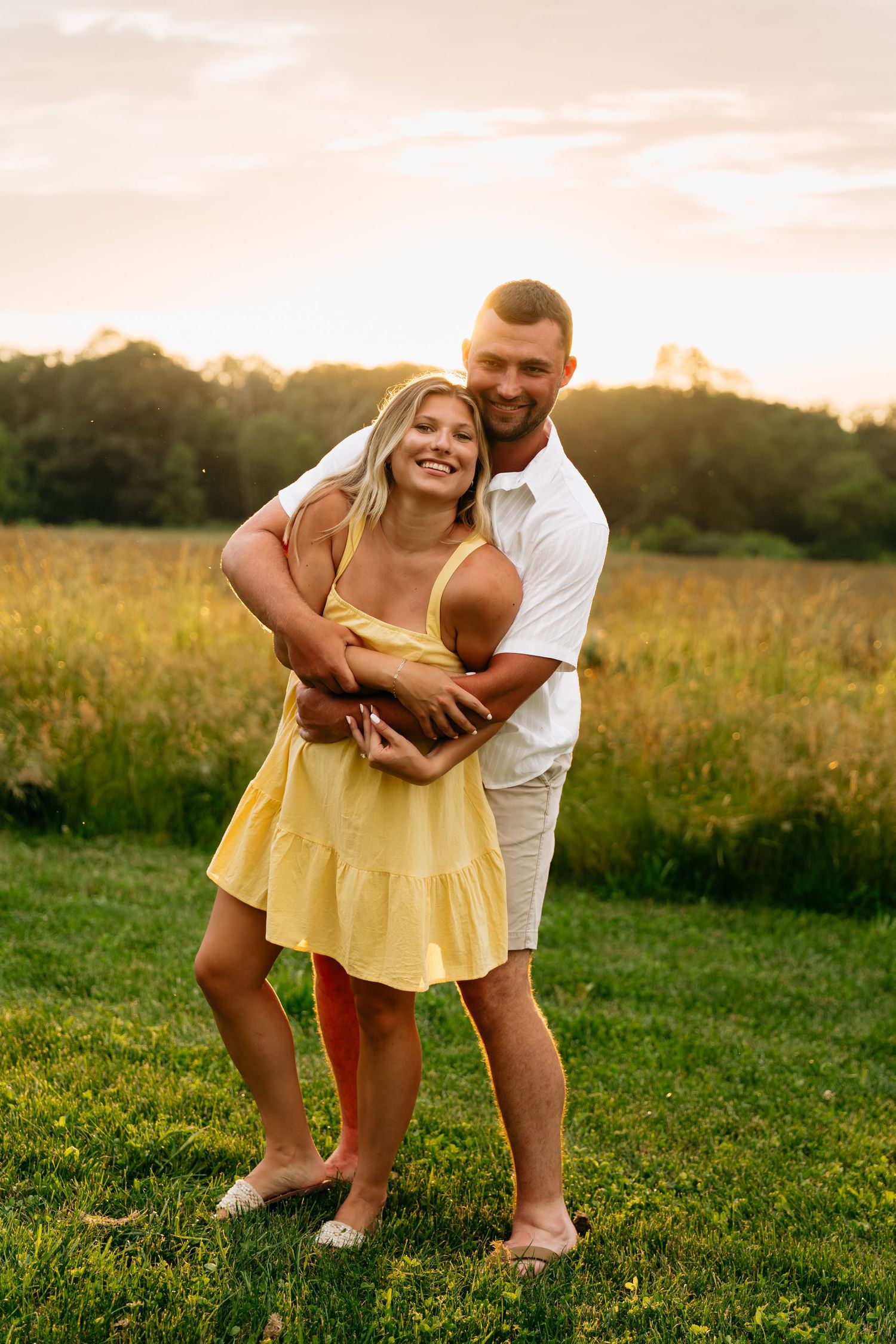 A couple shares playful moments in a golden meadow at sunset as they embrace and laugh together.