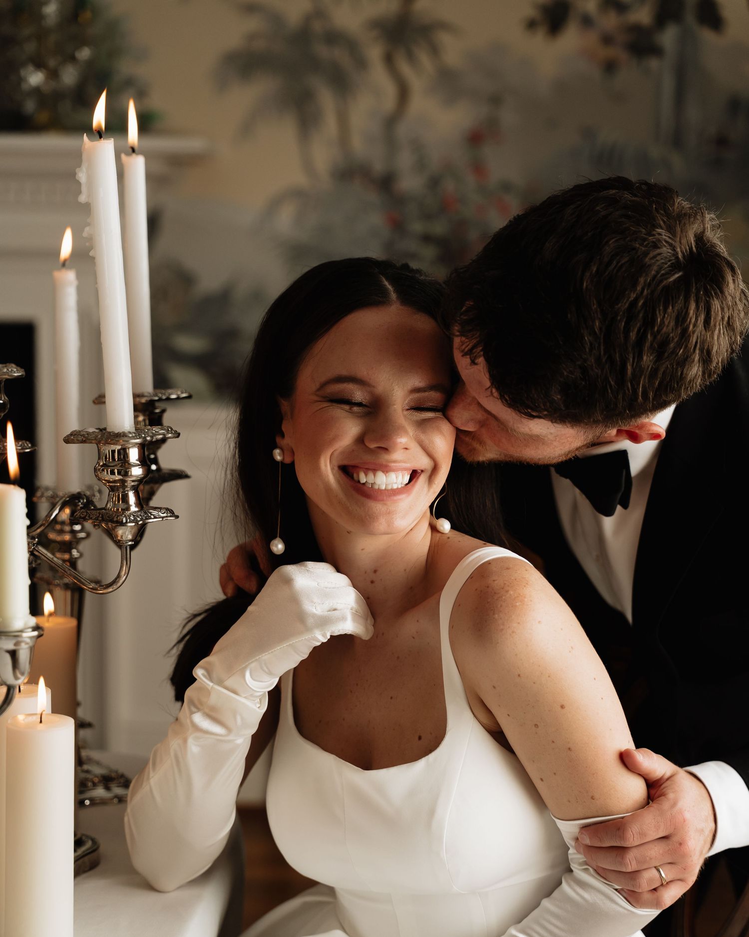 Romantic candlelit moment of couple in wedding attire sharing an intimate embrace at a decorated table.
