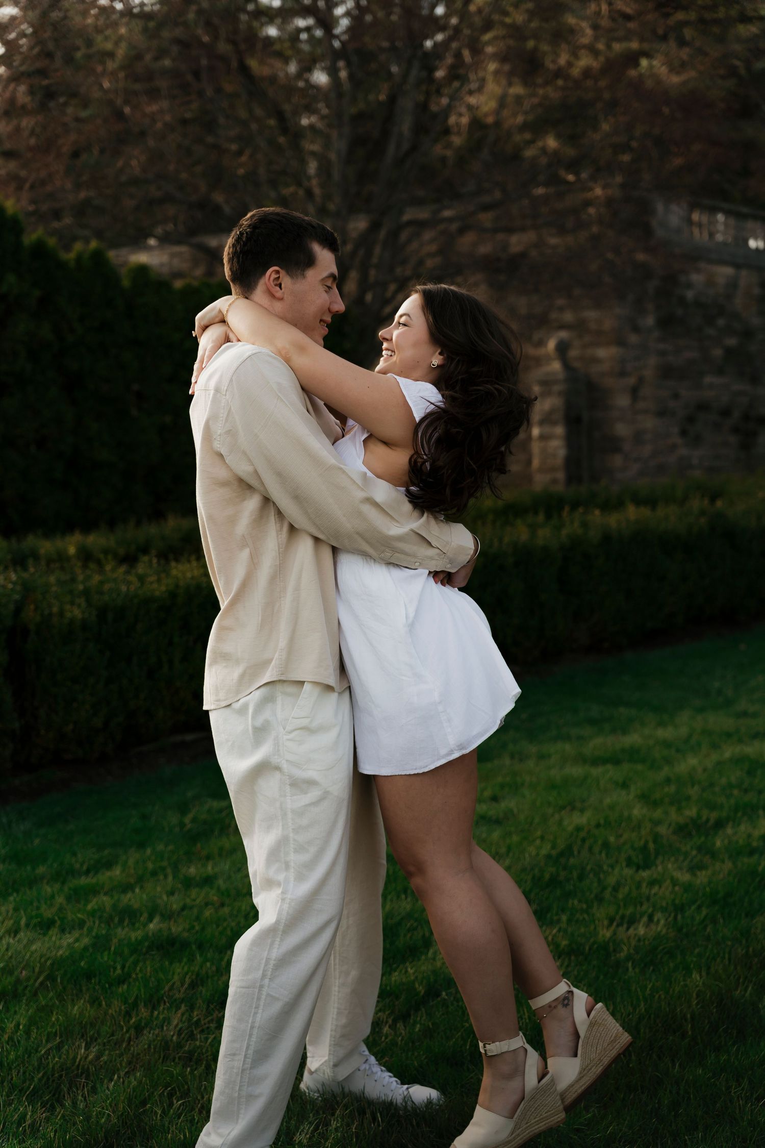 Elegant engagement portrait of couple in white outfits against 106-year-old estate garden in Loretto PA