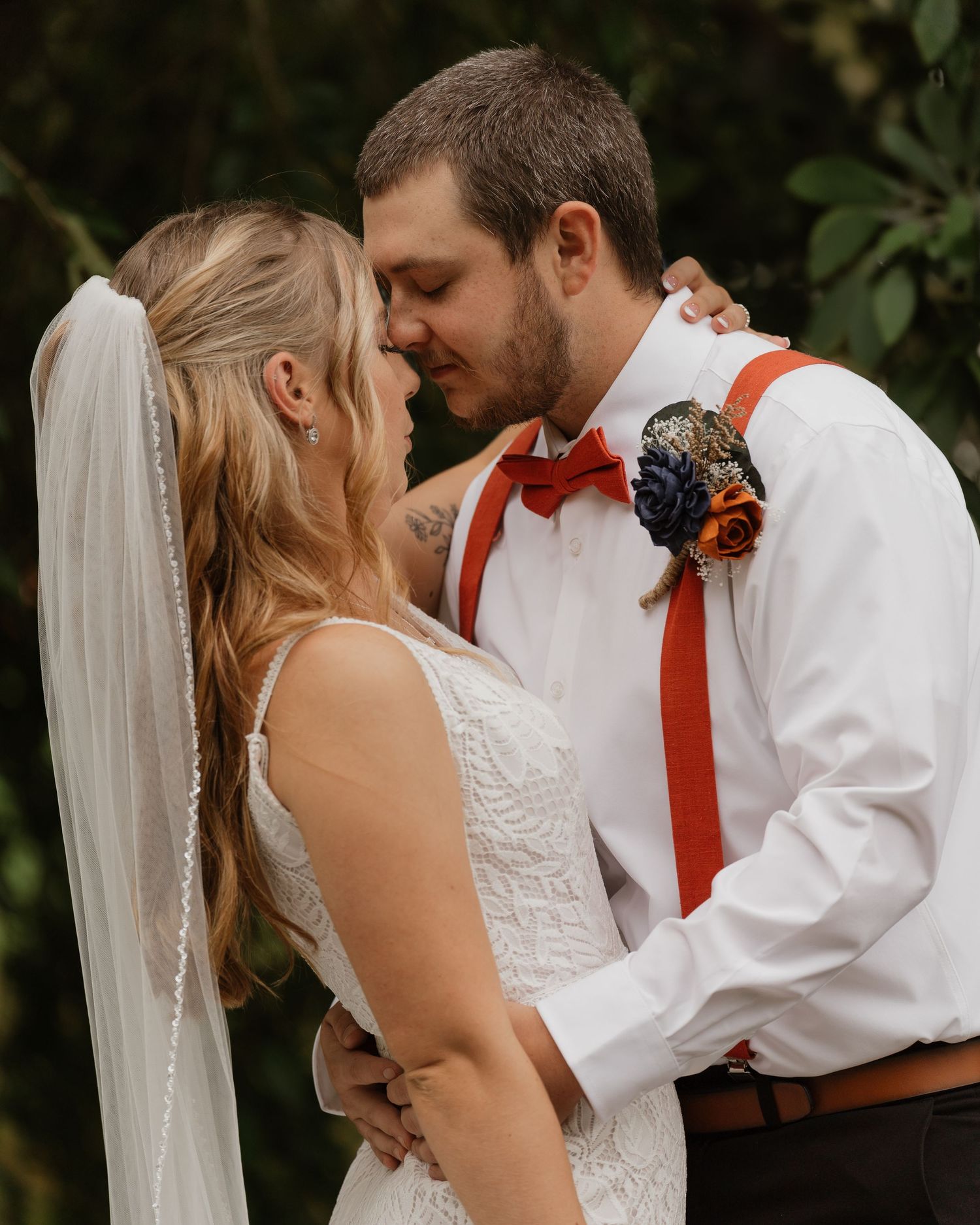 Intimate wedding portrait featuring autumn florals and rustic red suspender details.
