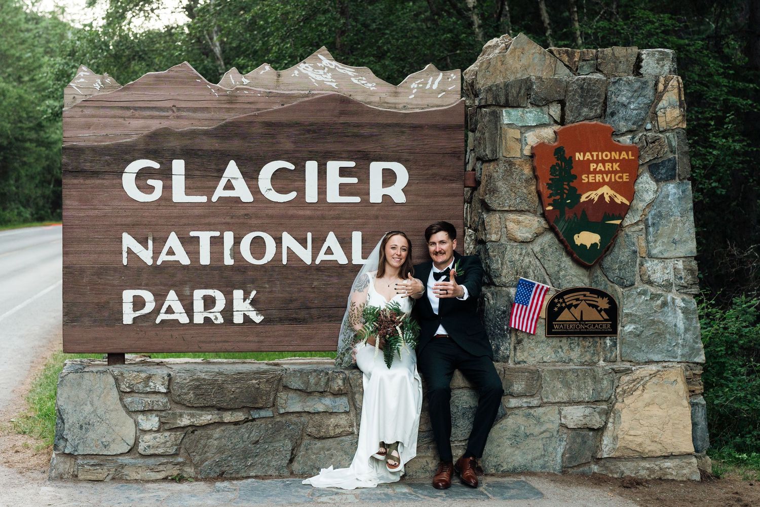 Couple in wedding attire toasting champagne at Glacier National Park entrance sign on their wedding day.