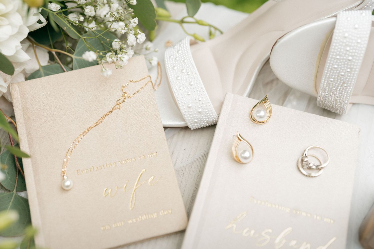 Elegant wedding flat lay with gold jewelry, pearl earrings, and Wife and Husband gift books on a soft neutral background.