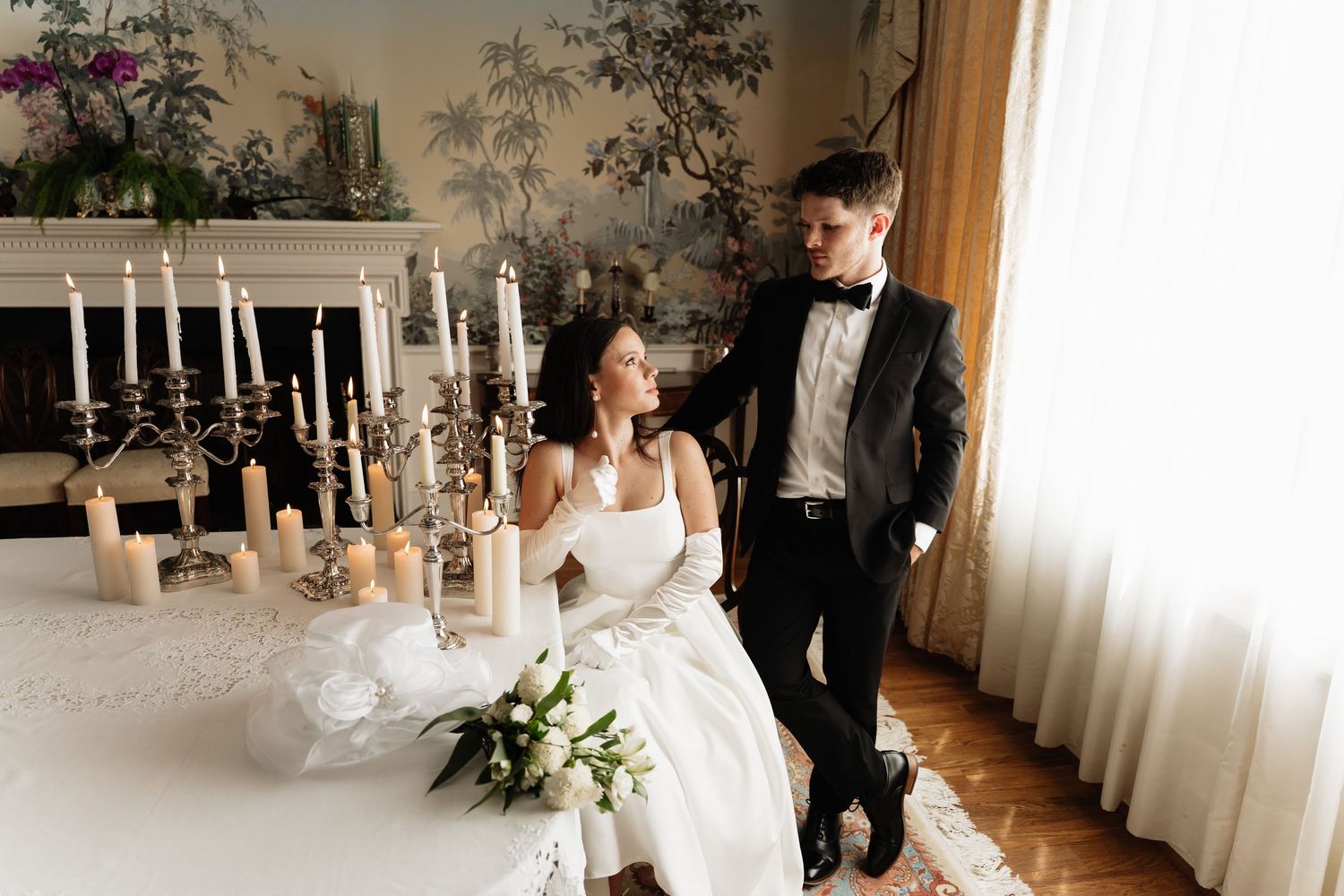 A romantic wedding scene with a couple at an elegant table decorated with white candles and floral arrangements.