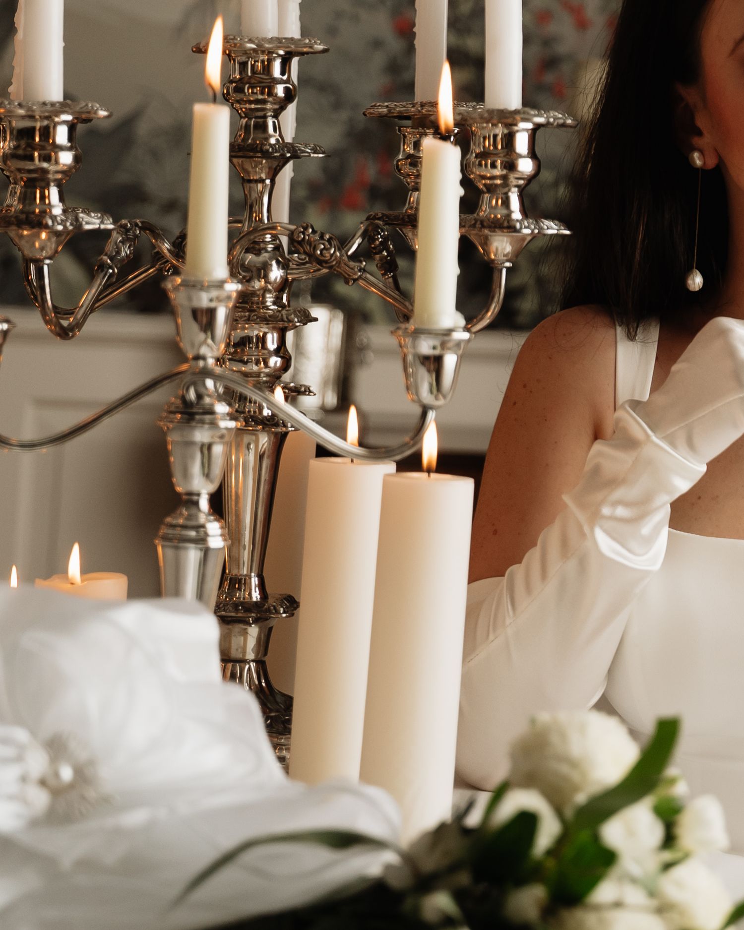 Elegant white candles burning in silver candelabras on a formal table setting with soft focus floral decorations.