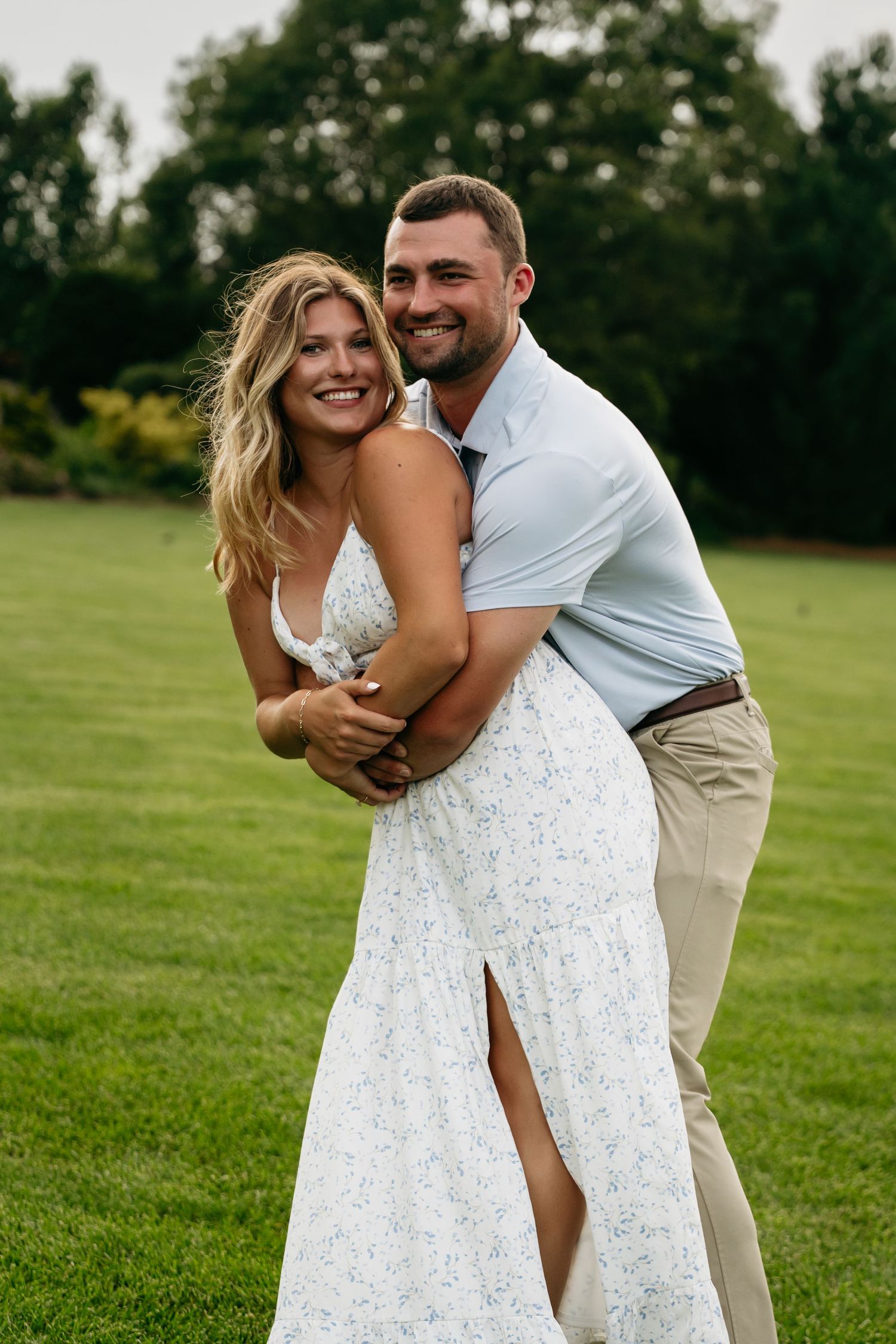A couple embraces joyfully on a green lawn, with the person in a flowing white lace dress dancing and twirling.
