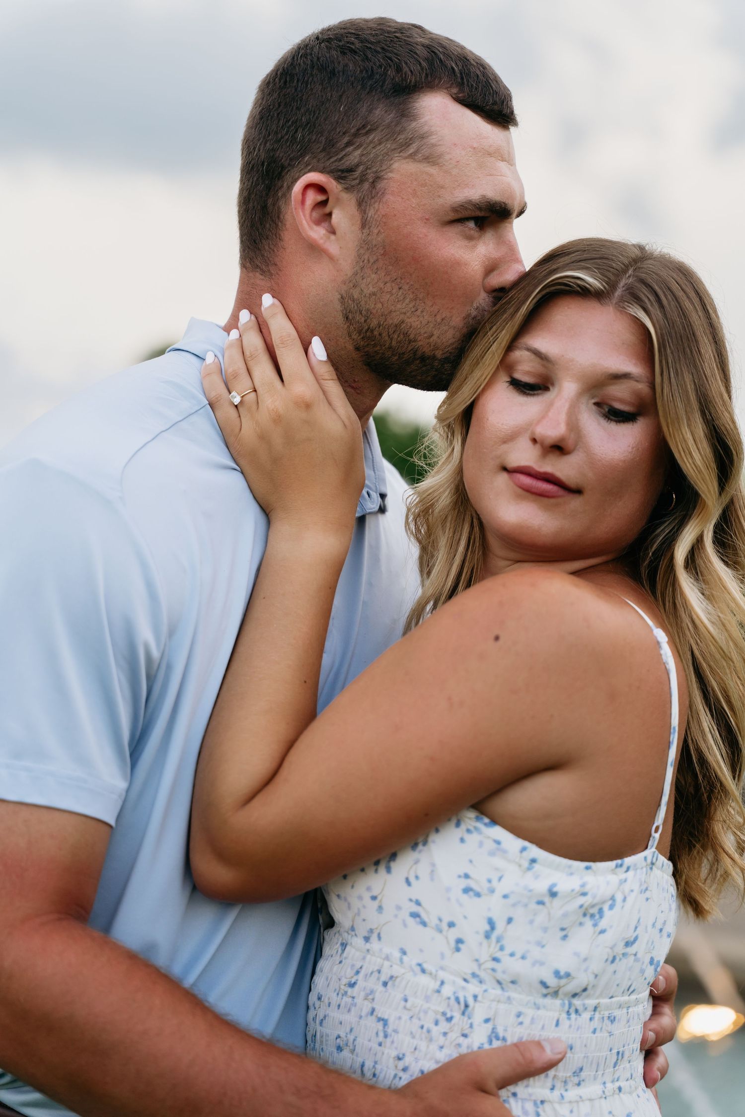 Romantic couple in an intimate embrace outdoors with woman wearing a blue and white floral dress.
