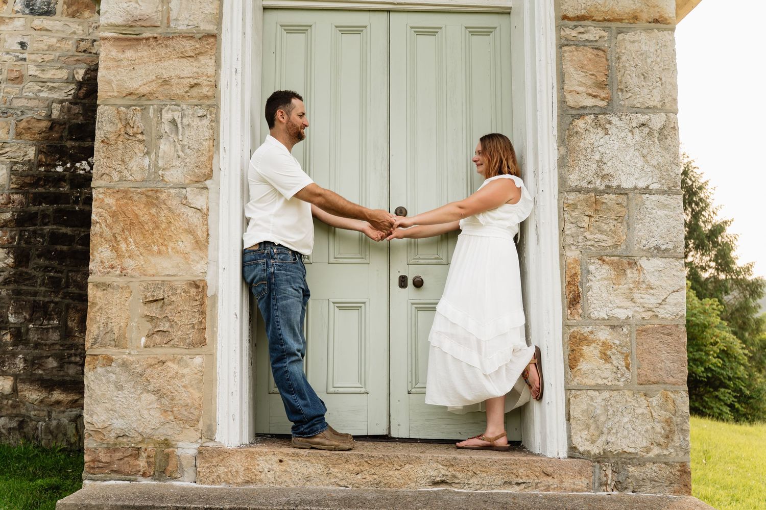 A couple shares a playful moment while standing at a vintage light blue door of a stone building.