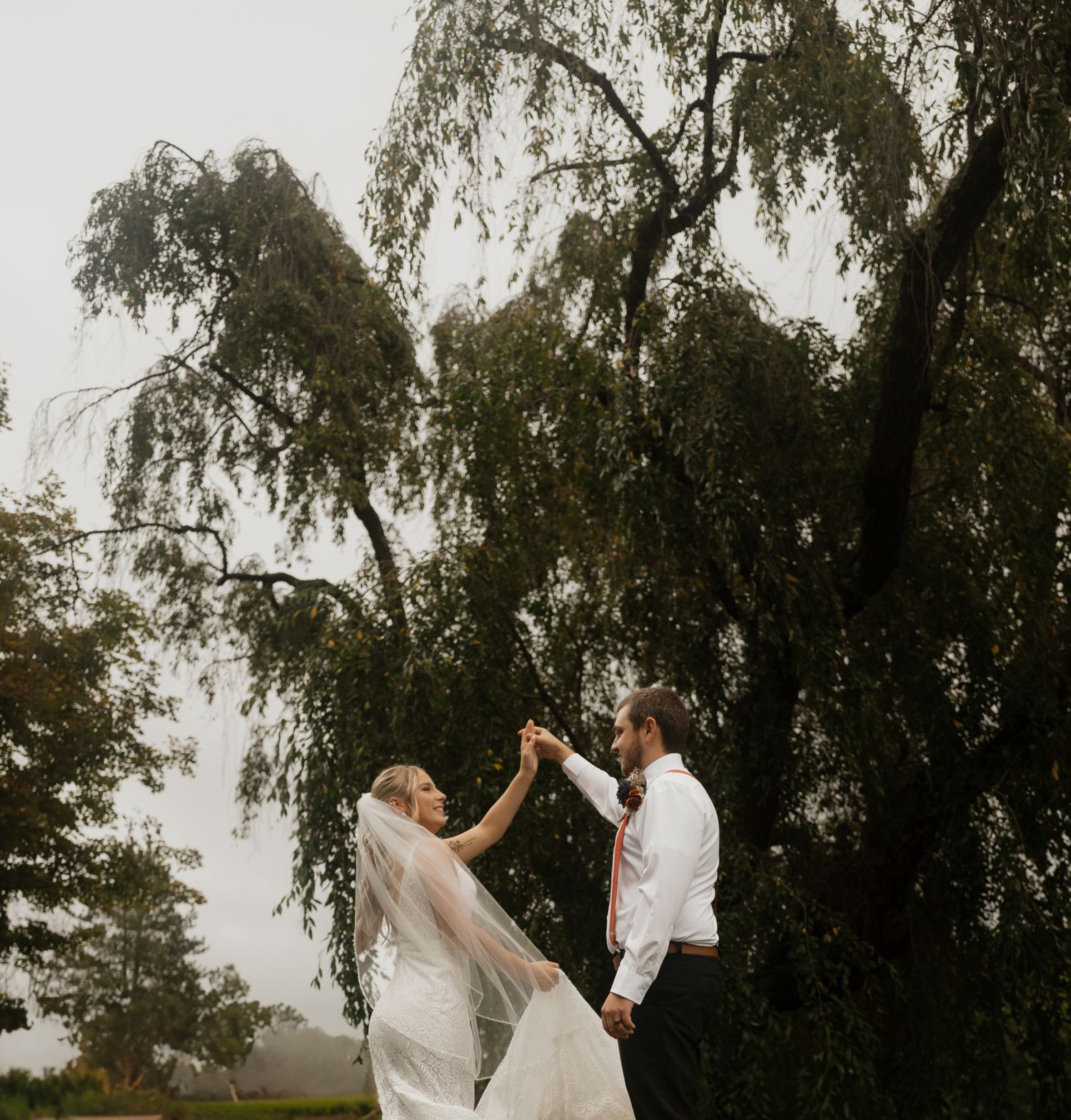 Wedding couple dancing under weeping willow trees in romantic outdoor setting.