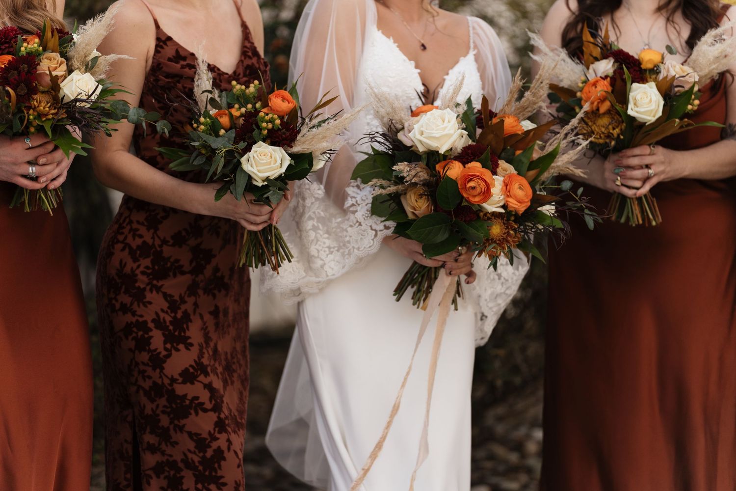 Fall wedding bouquets featuring orange and white flowers with rich burgundy accents held by bridesmaids.