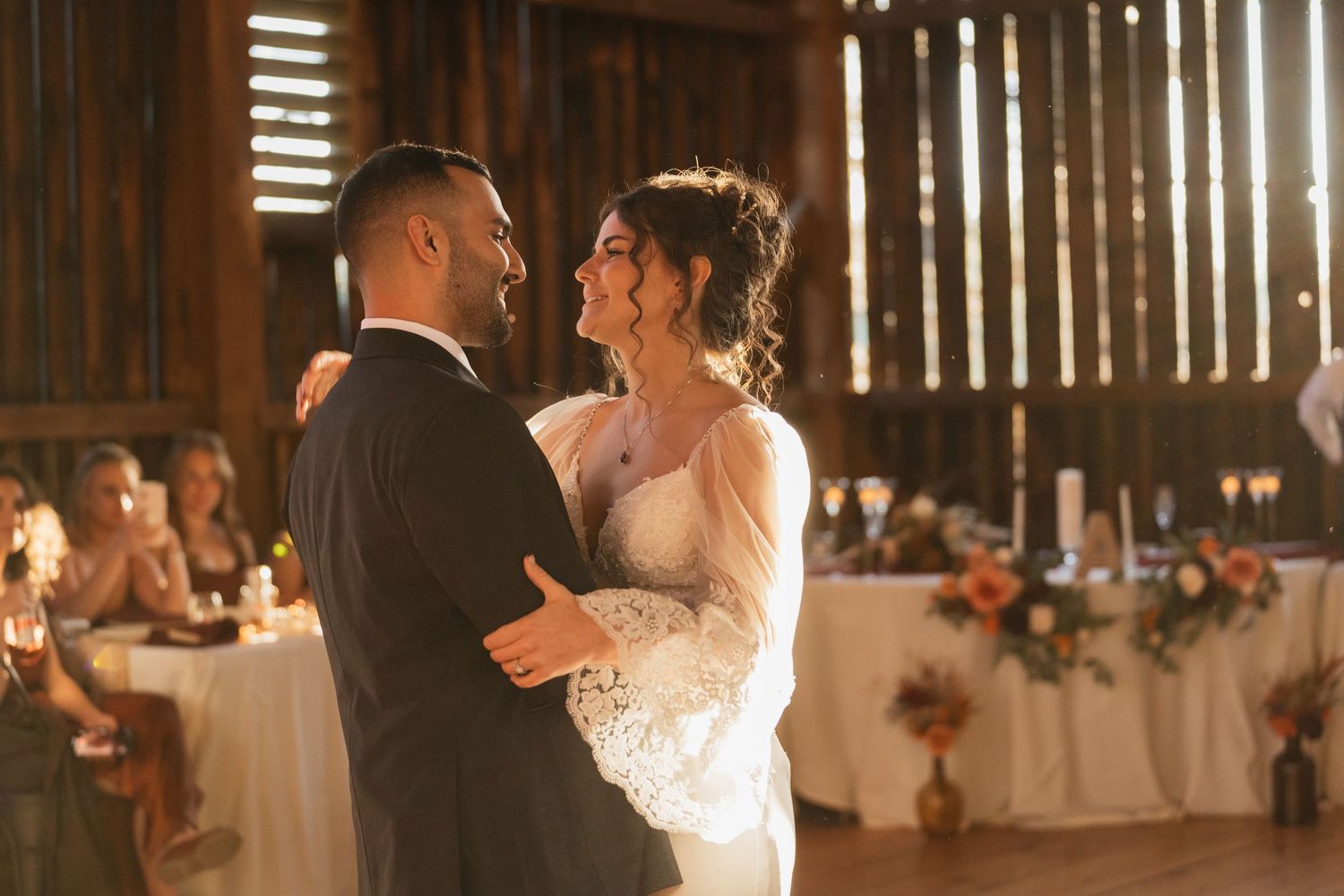Wedding reception takes place in rustic barn venue with atmospheric lighting creating a warm ambiance.