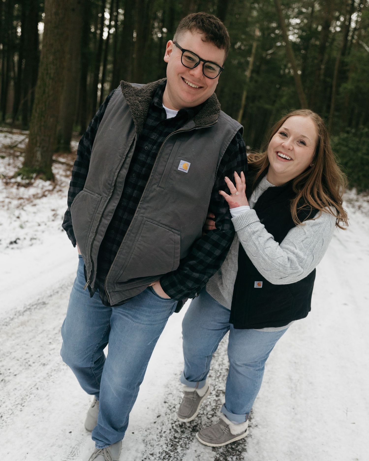 A cheerful couple posing together on a snowy forest path.