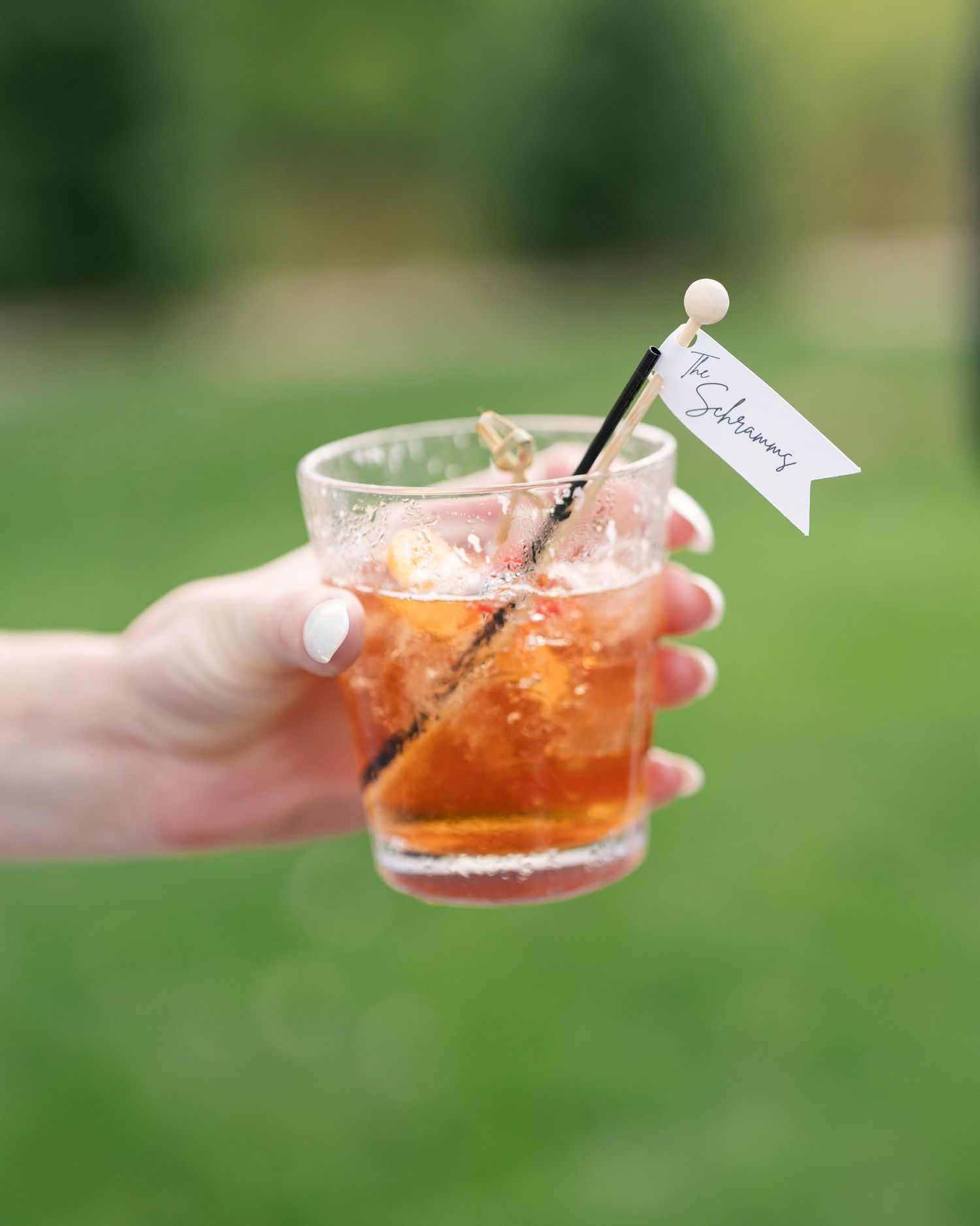 Hand holding a cocktail glass with an orange drink garnished with a small white flag stirrer outdoors.