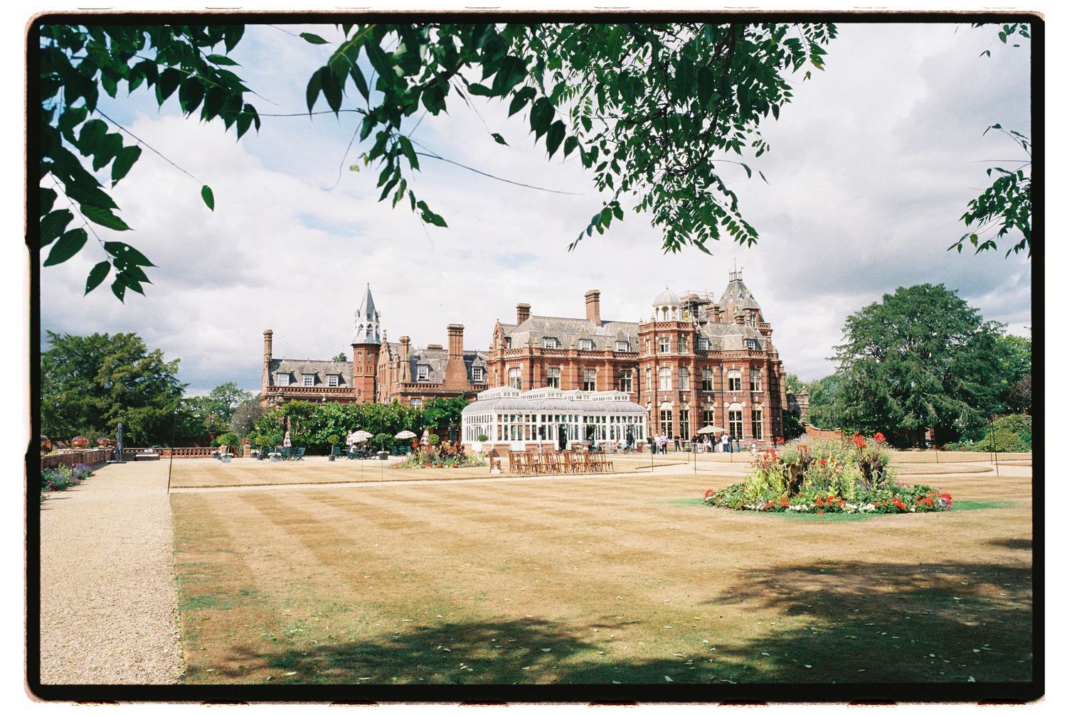 Grand Victorian red-brick country house hotel with manicured lawns and gardens under a cloudy summer sky.