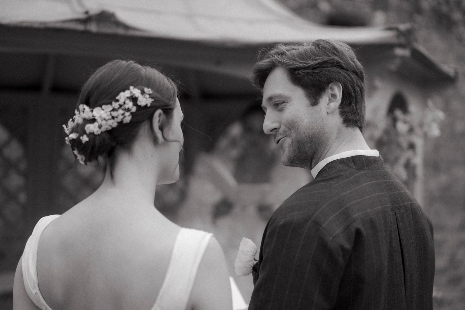 Black and white wedding photo of a smiling groom in a pinstripe suit beside a bride wearing a delicate floral hair piece.