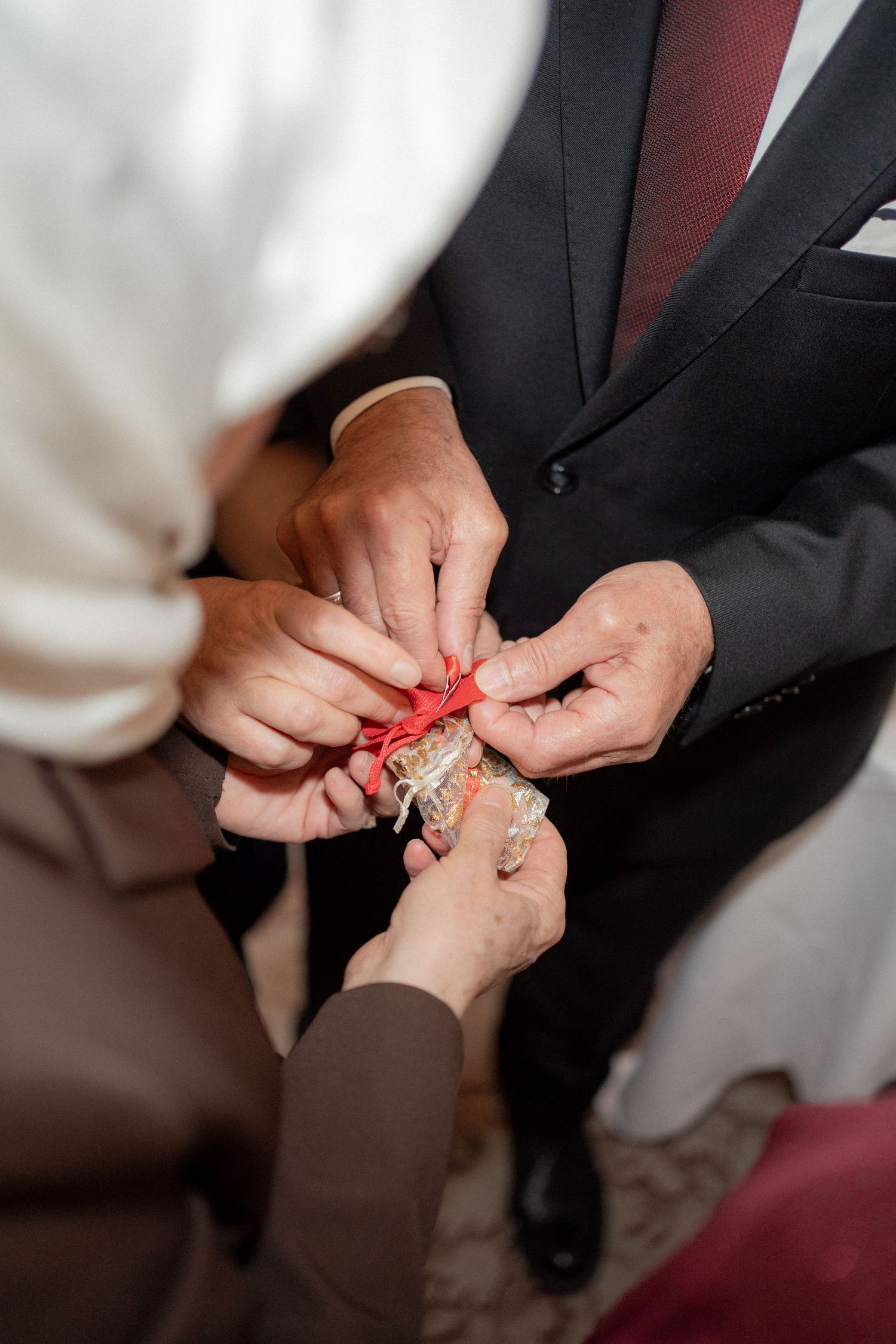 Close-up of hands exchanging or tying something with a red ribbon during a wedding ceremony.