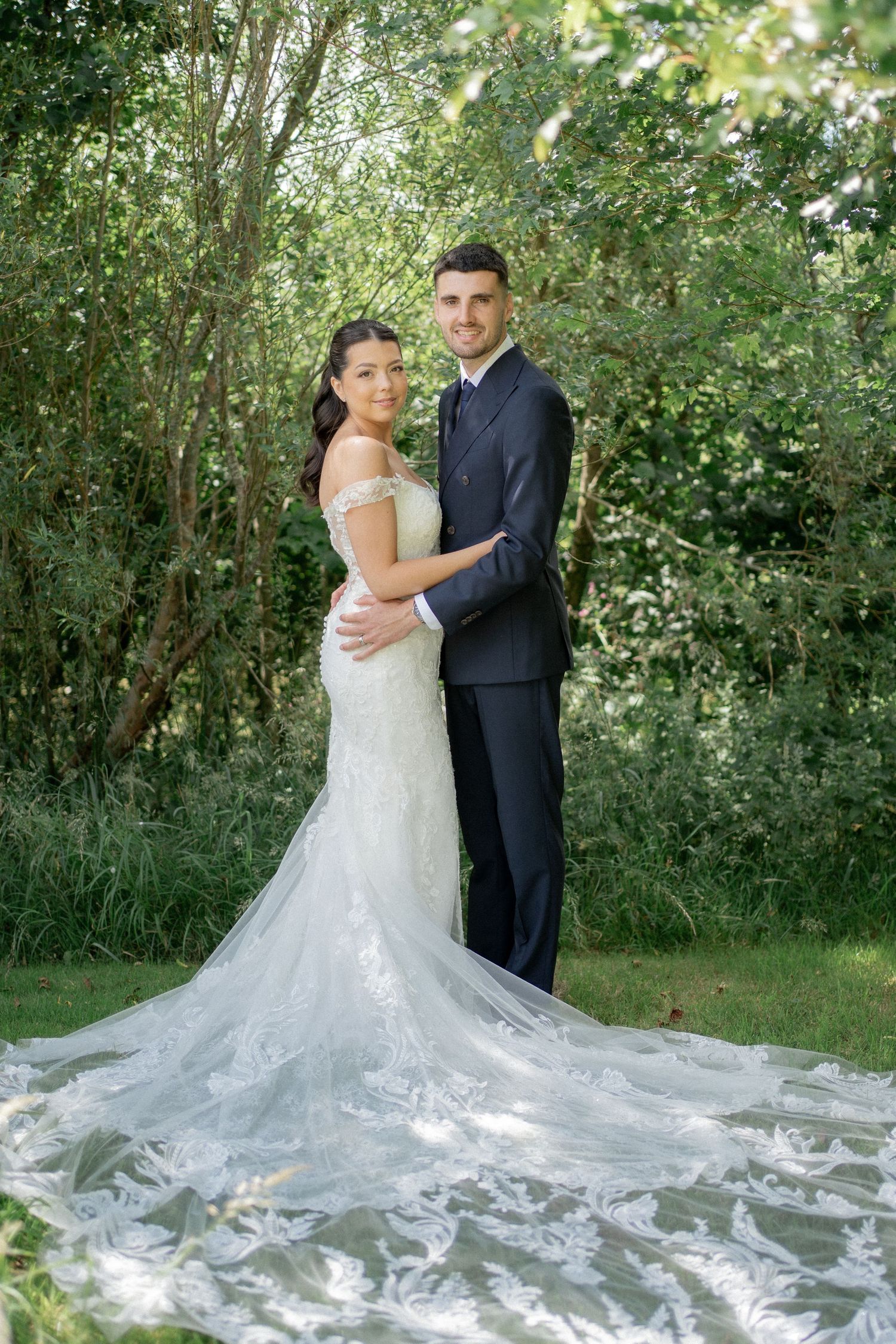 Wedding couple posing in a garden setting with a dramatic cathedral-length lace train.
