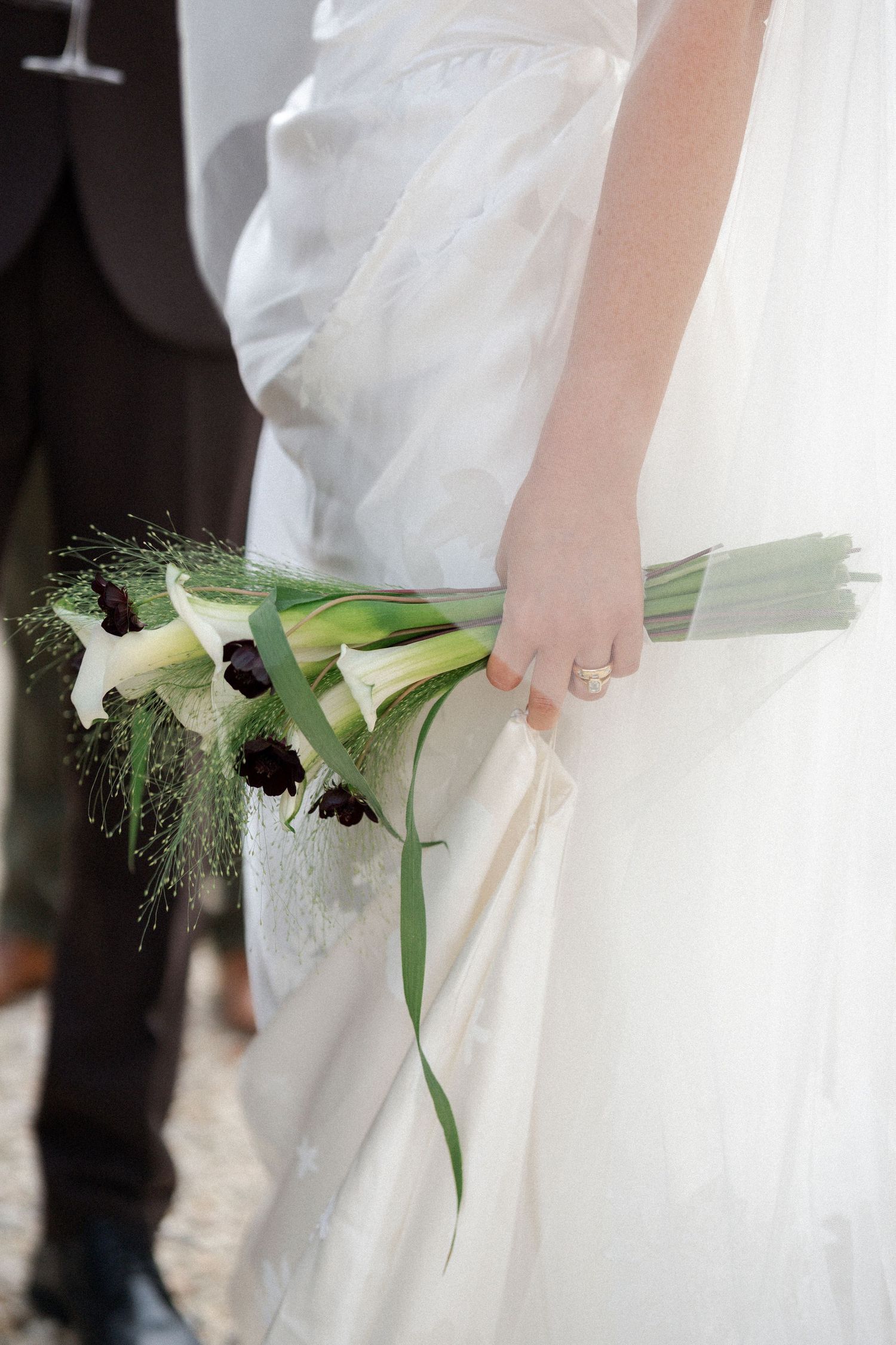 Bride in white gown holds a bouquet of calla lilies at her wedding.