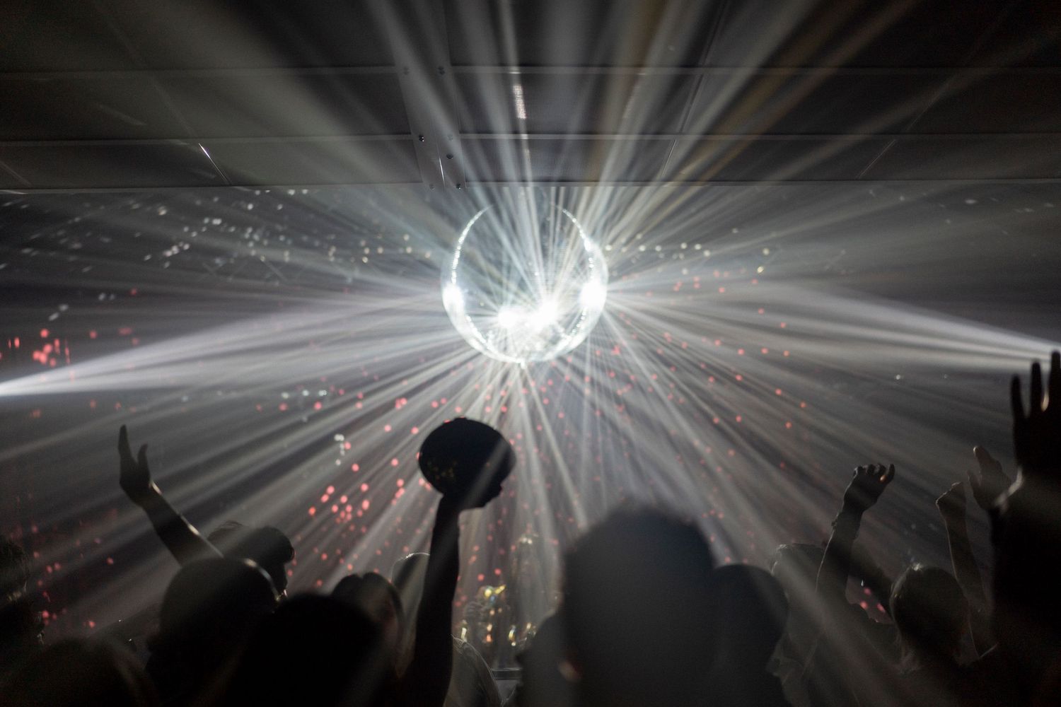 A glowing disco ball scatters beams of light over a dancing crowd with raised hands at a lively wedding reception party.