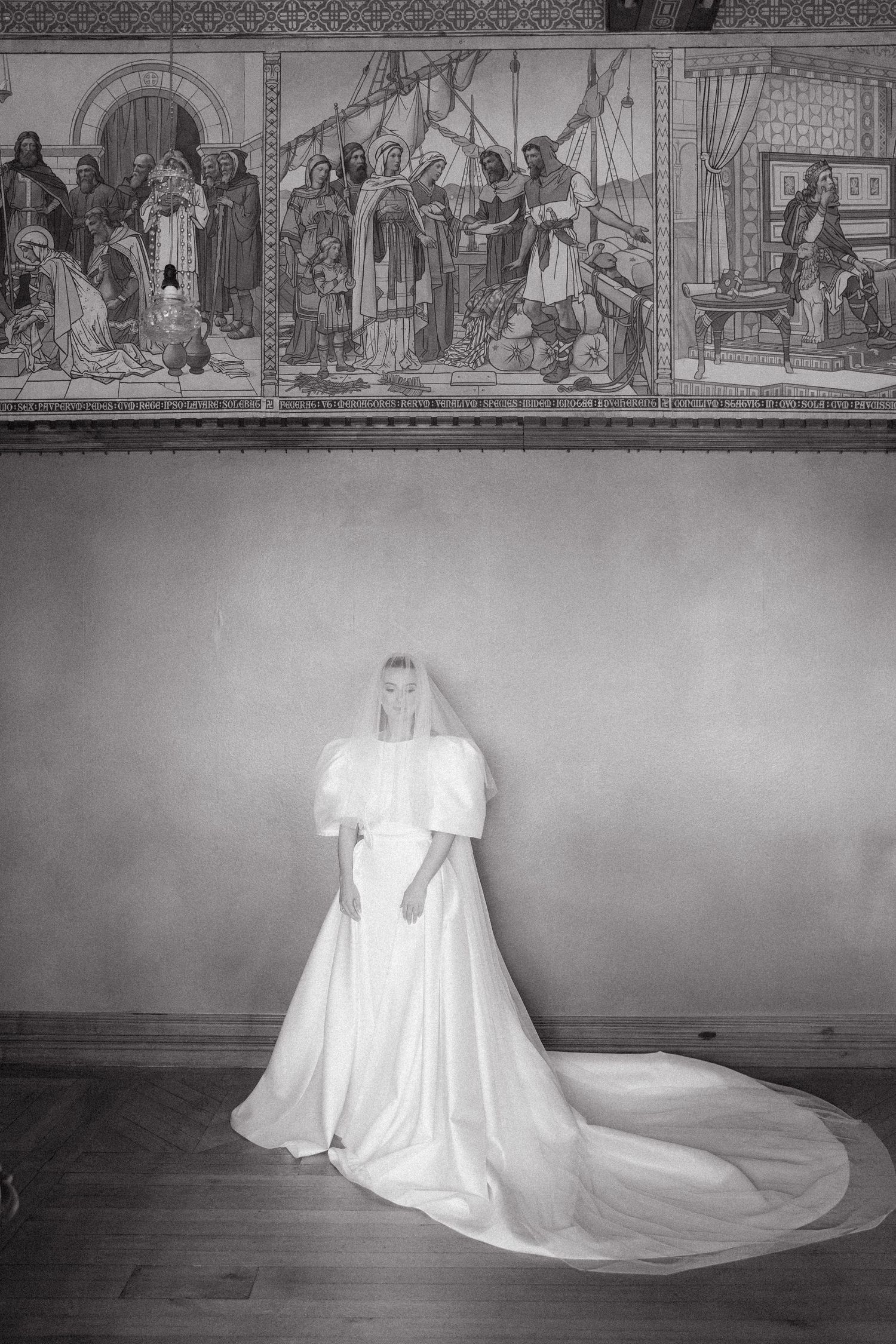 Black and white artistic wedding dress photo with flowing train against decorative wall murals.