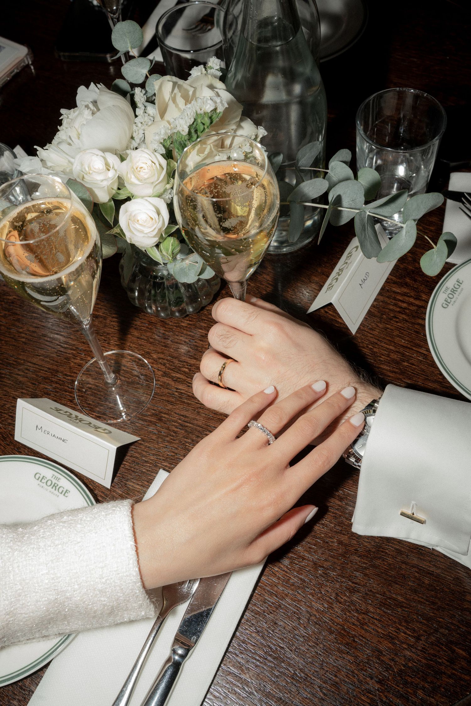 Close-up shots of hands with rings and white floral arrangements on a dark wooden table.