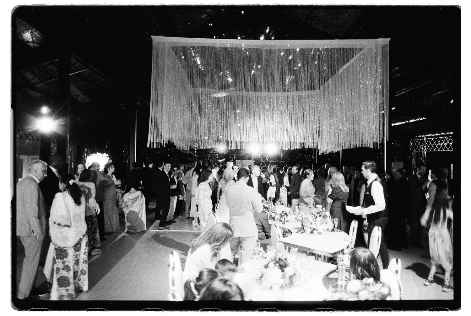 Black and white photo of wedding reception with couple dancing under a stunning crystal fringe canopy centerpiece.