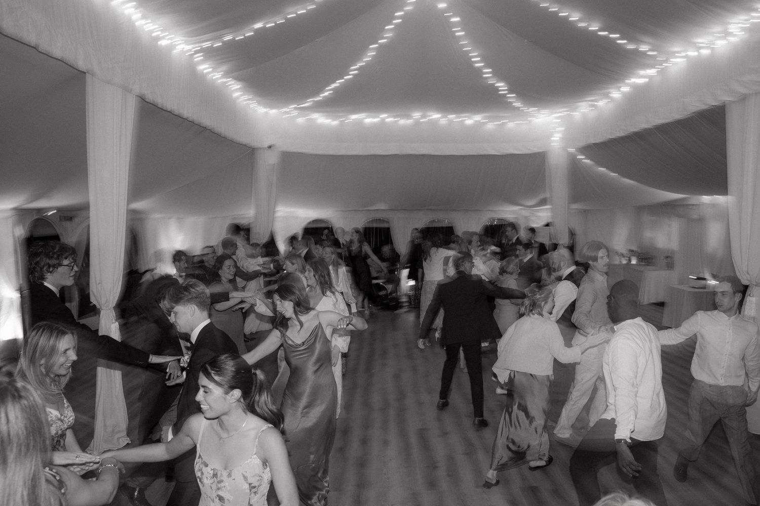 People dance together in a dimly lit room decorated with string lights during a social gathering.
