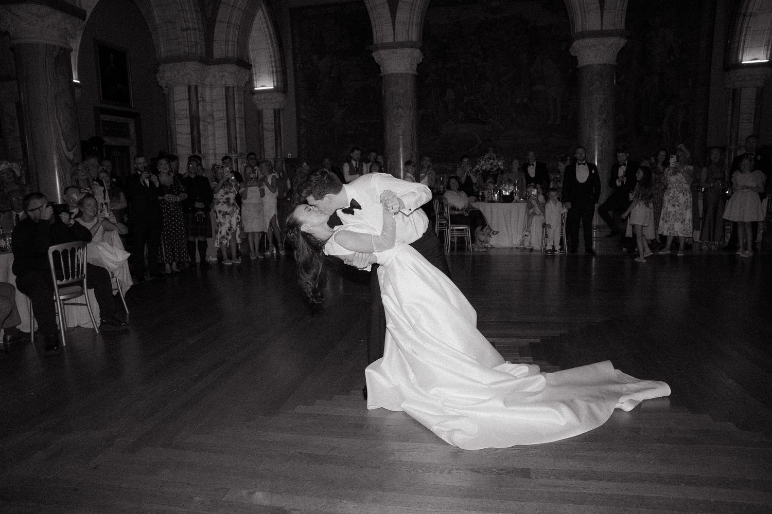 A dramatic black and white photo of a wedding couple's first dance, with the bride's dress flowing elegantly across the ballroom floor.
