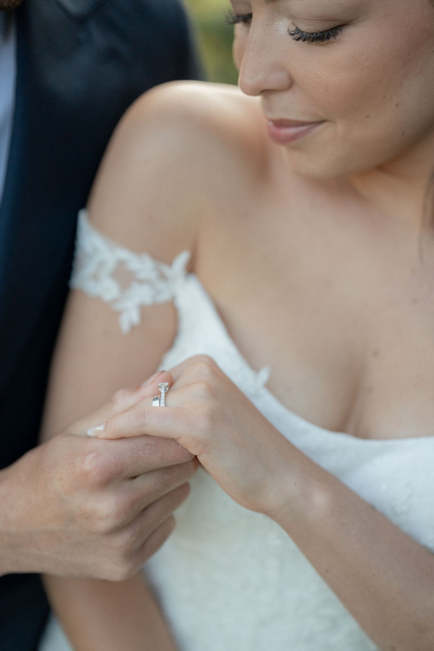 Close-up shot of hands exchanging wedding rings with lace dress detail.