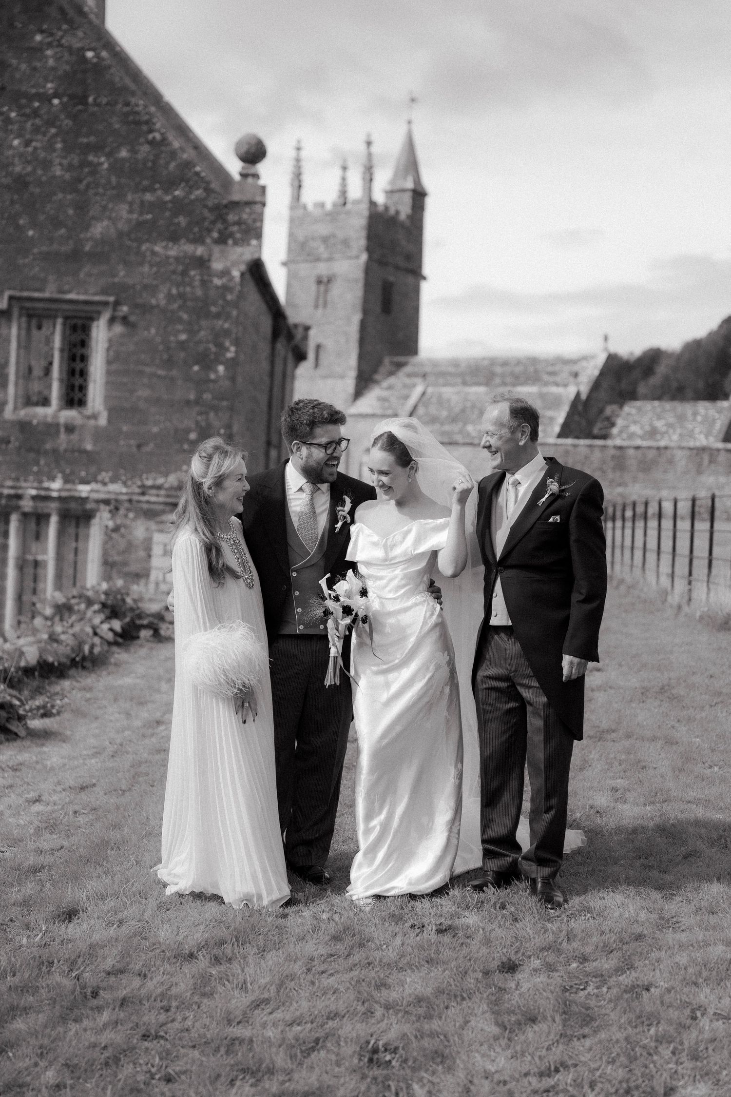 Bride and groom pose with family members outside historic stone church in classic black and white photo.
