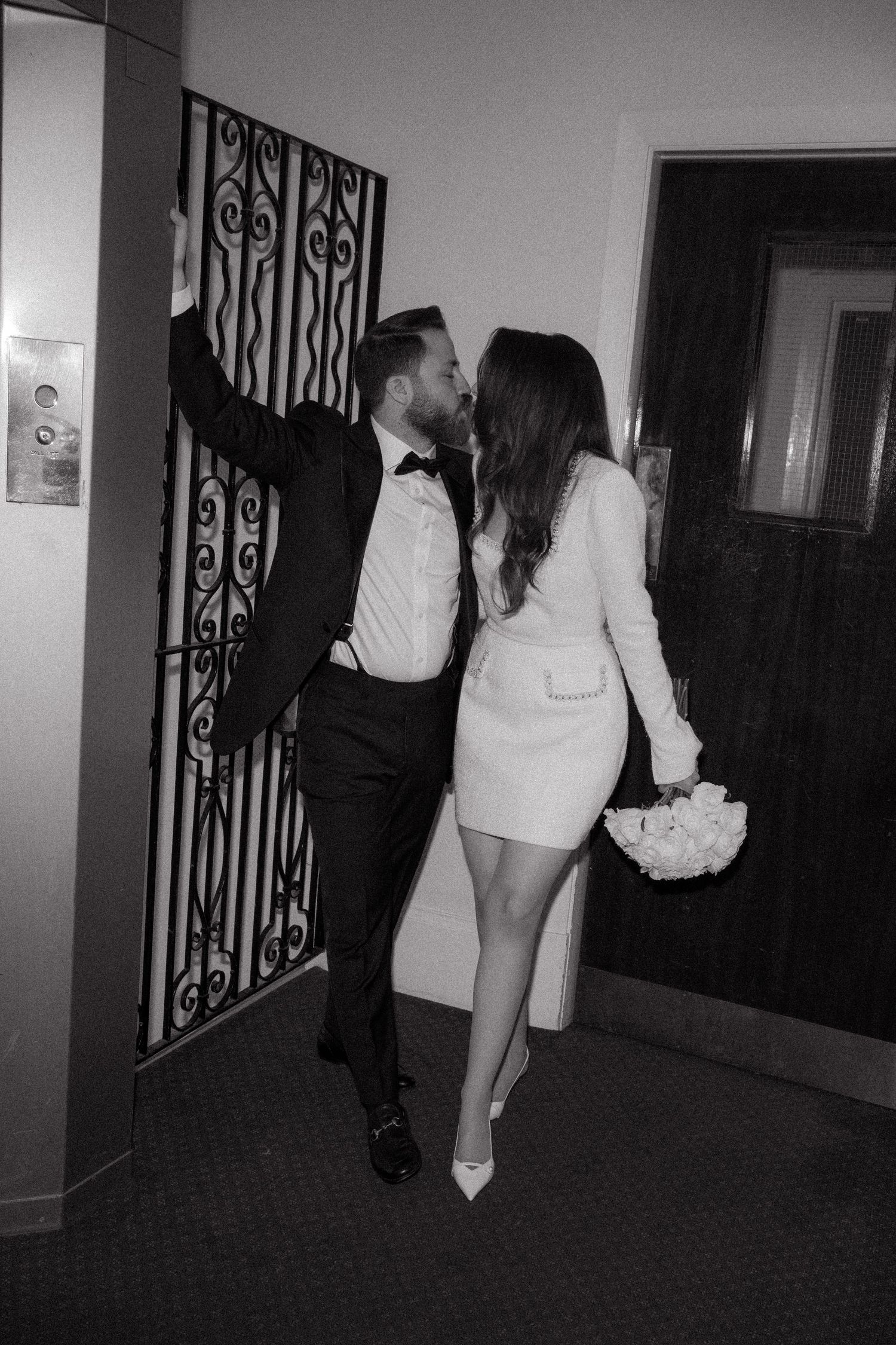 A couple walks down a dimly lit hotel hallway in formal wedding attire.