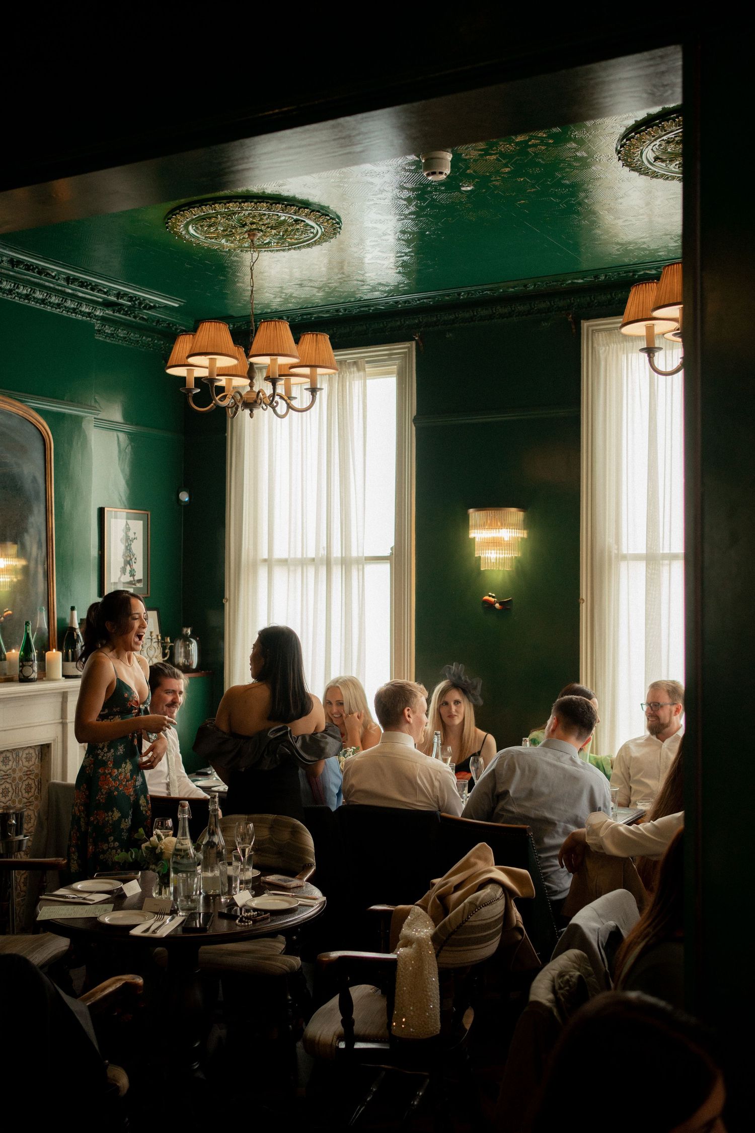 Atmospheric dining room with dark green walls and elegant lighting where guests are gathered.