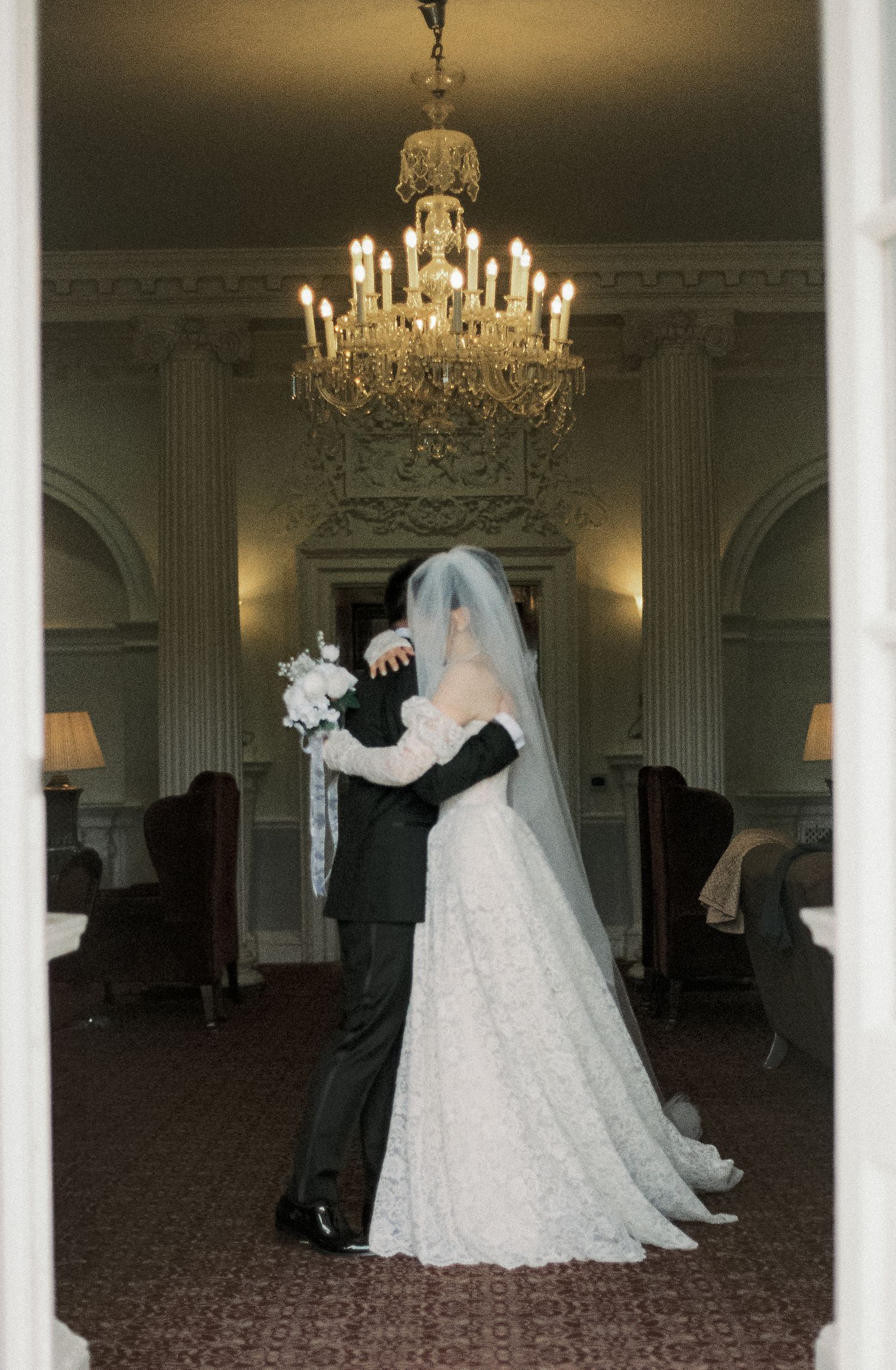 Wedding couple dancing in elegant ballroom under crystal chandeliers.