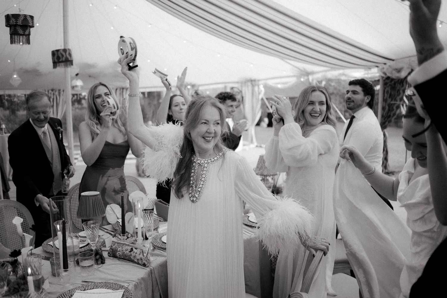 Joyful wedding guest in white dress celebrates with raised arms at elegant marquee reception.