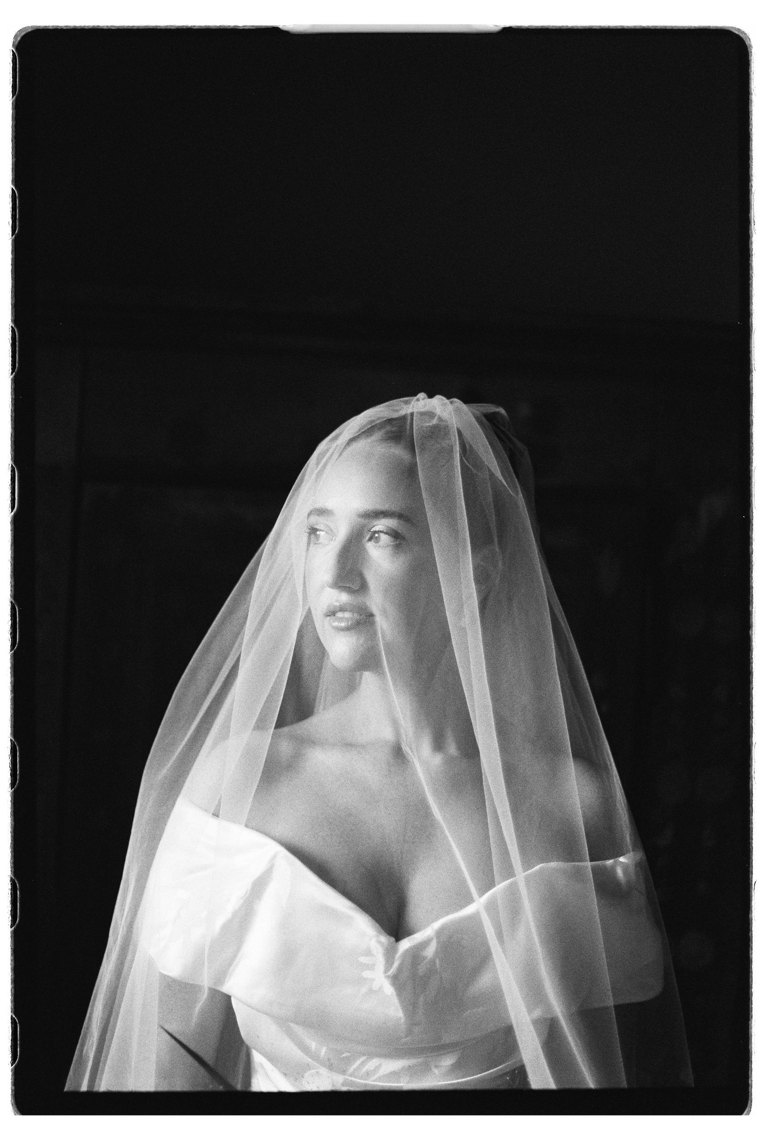 Ethereal black and white portrait of a bride wearing a flowing veil and off-shoulder wedding gown.