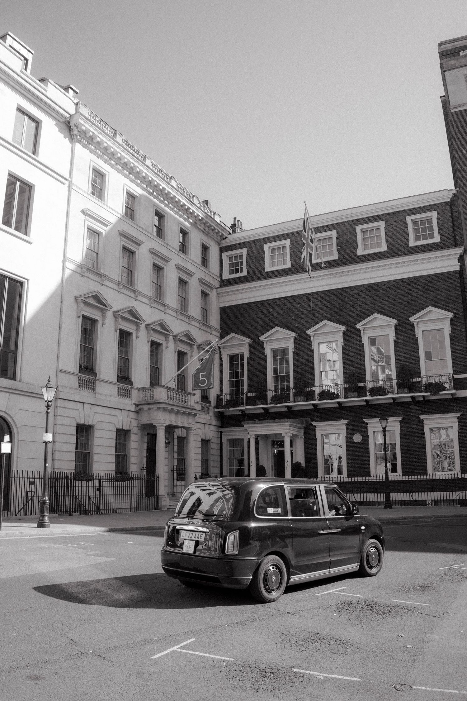 Black and white photo of a classic London black cab parked on a quiet street with historic Georgian buildings.