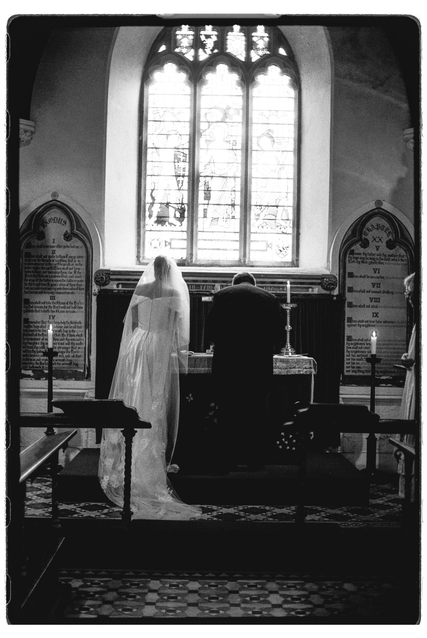 Bride and groom kneeling at church altar during wedding ceremony, black and white photography.