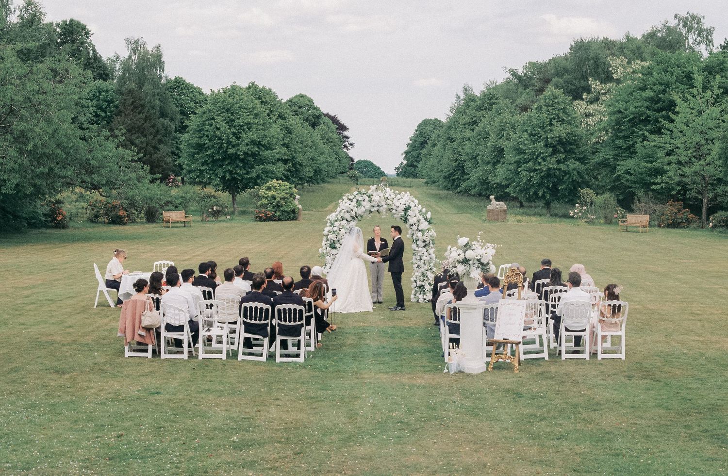 Panoramic view of outdoor wedding ceremony setup with white chairs on green lawn.
