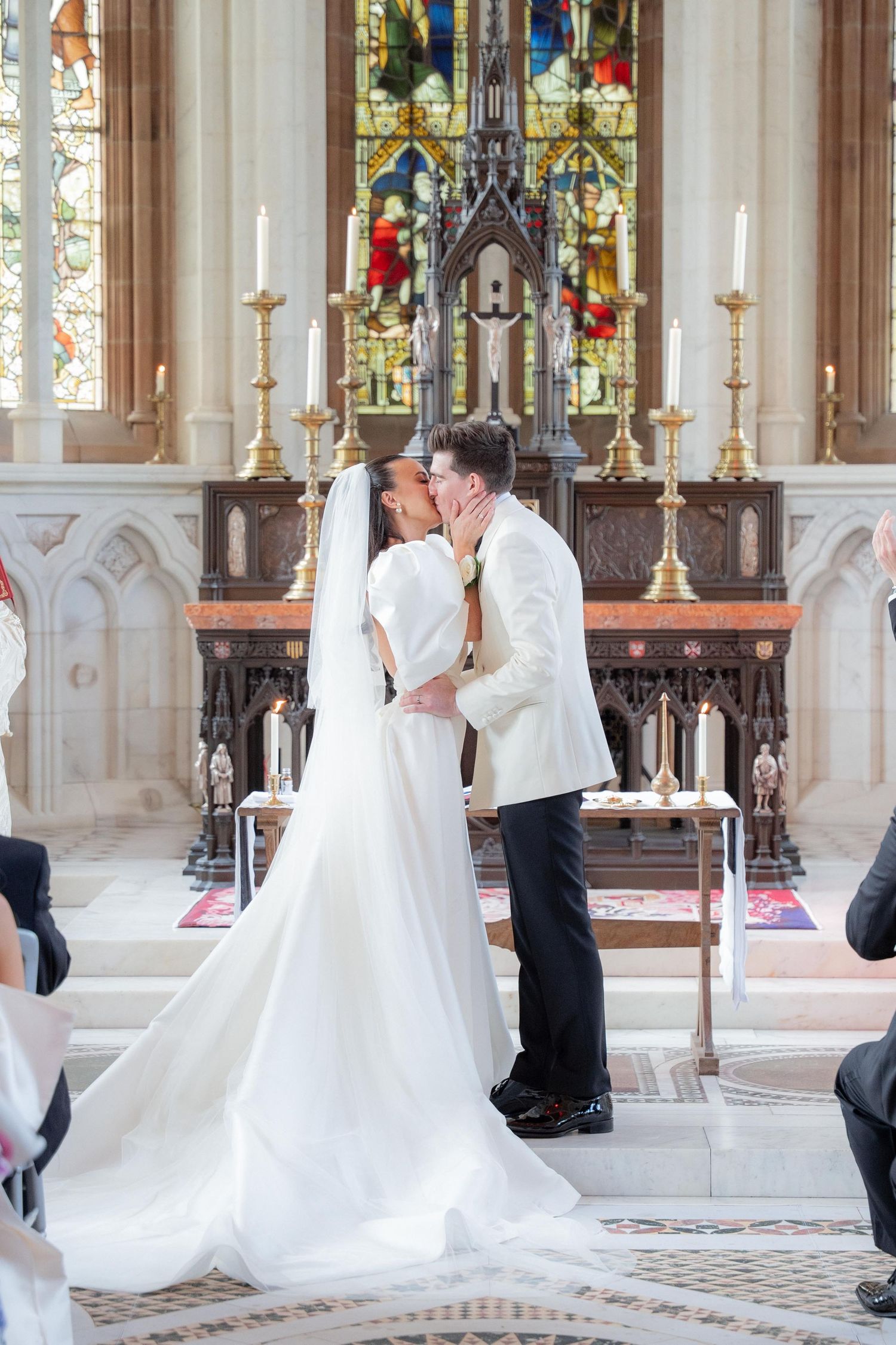 Wedding ceremony in ornate church with stained glass windows and traditional altar decorations.