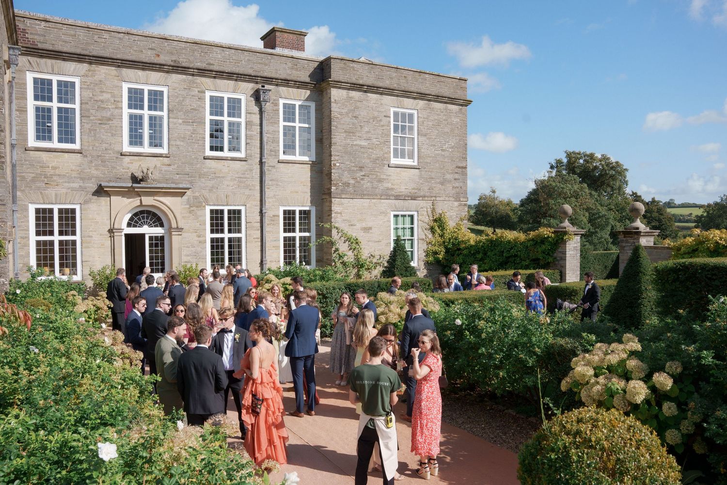 Wedding guests gather outside a historic stone manor house during an elegant outdoor celebration in the countryside.