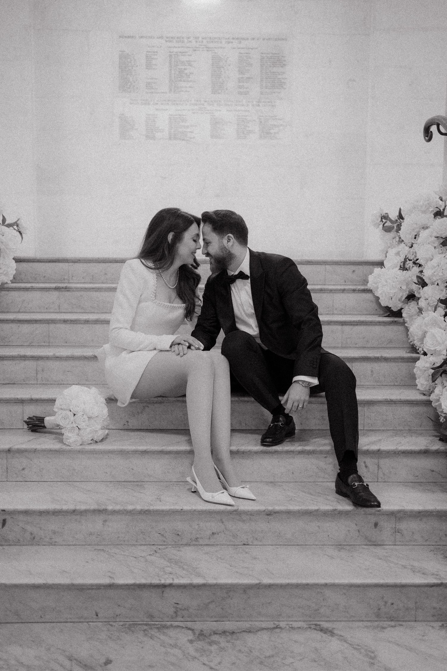 A romantic black and white photo sequence shows a couple sharing a kiss while sitting on marble steps with floral decorations.