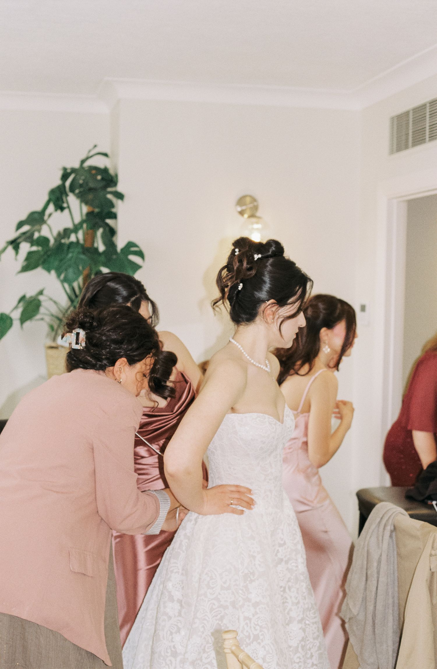 Wedding preparations with bridesmaids helping with final touches in white room.