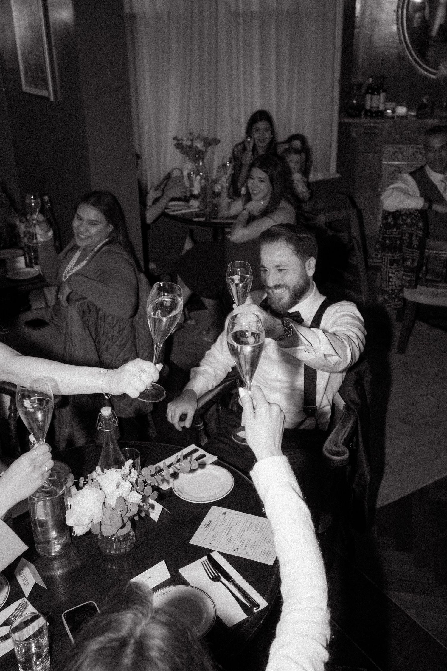Wedding reception guests raising glasses in celebration at a dimly lit venue.